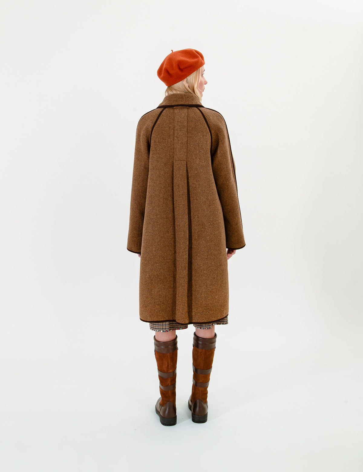 Woman wearing a brown coat, red beret, and brown boots on a white background