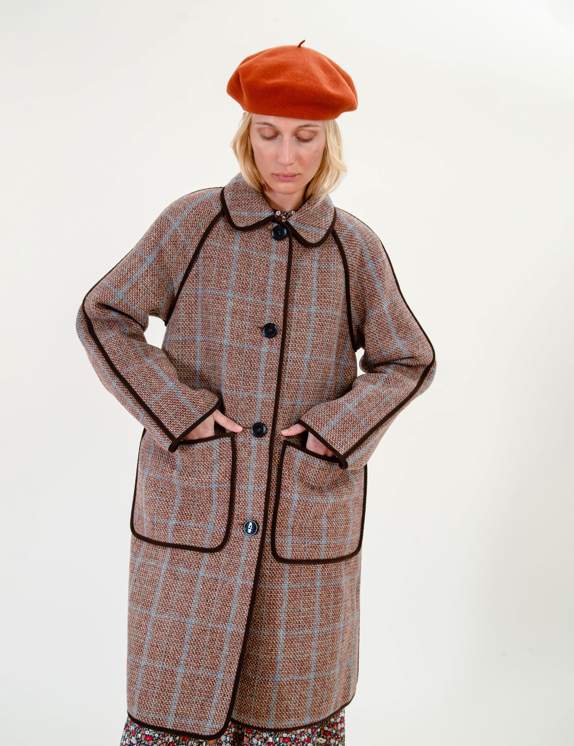Woman wearing a brown plaid coat and orange beret on a white background