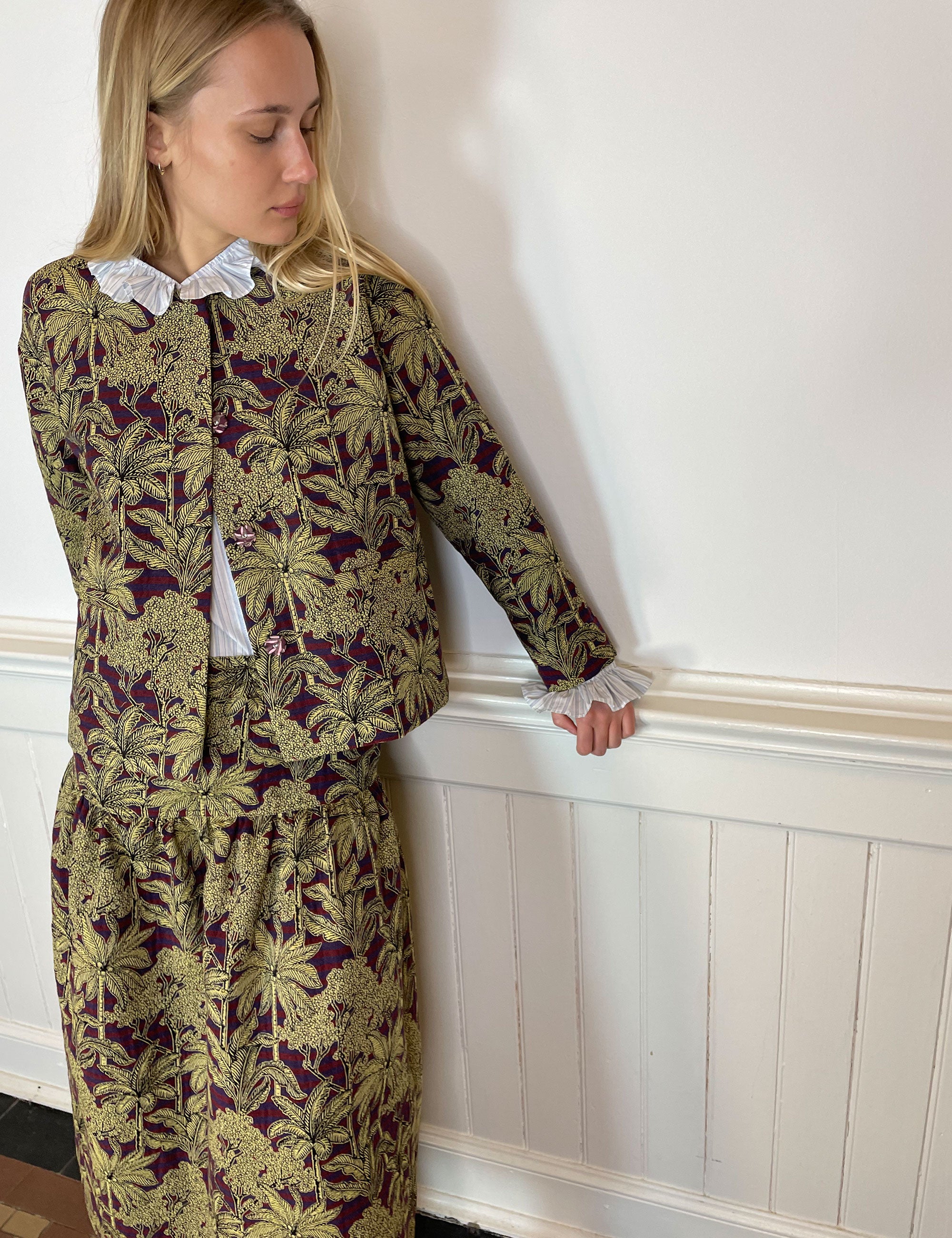 Woman in jacquard jacket and skirt with red and blue stripes and golden palm print