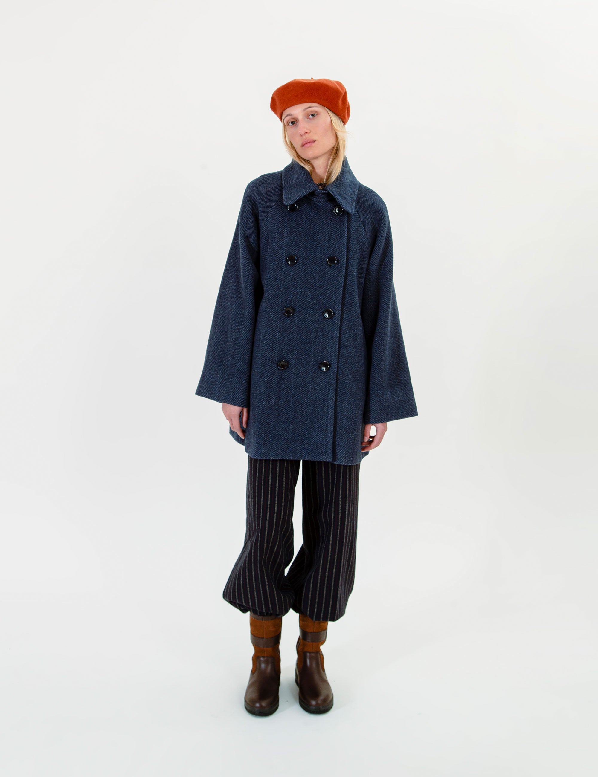 Woman wearing a blue wool jacket, striped pants, and a red beret on a white background