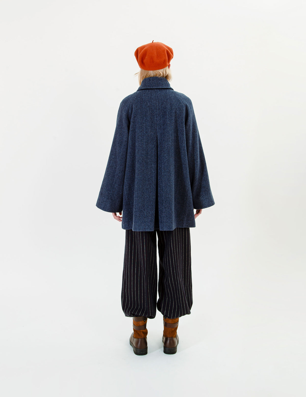 Woman wearing a blue wool jacket, striped pants, and a red beret on a white background