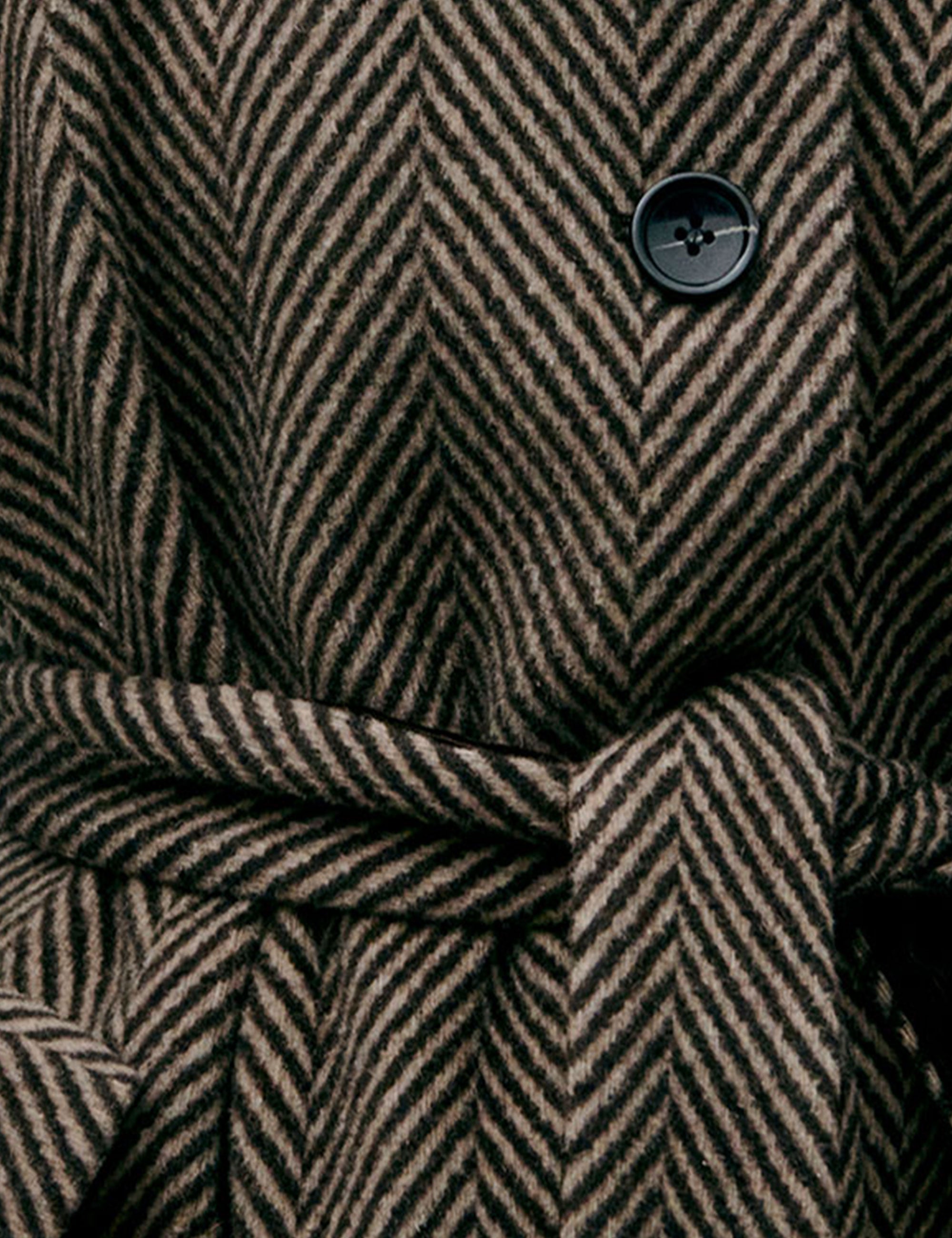 Close-up of a herringbone-patterned women's coat with a button and belt.