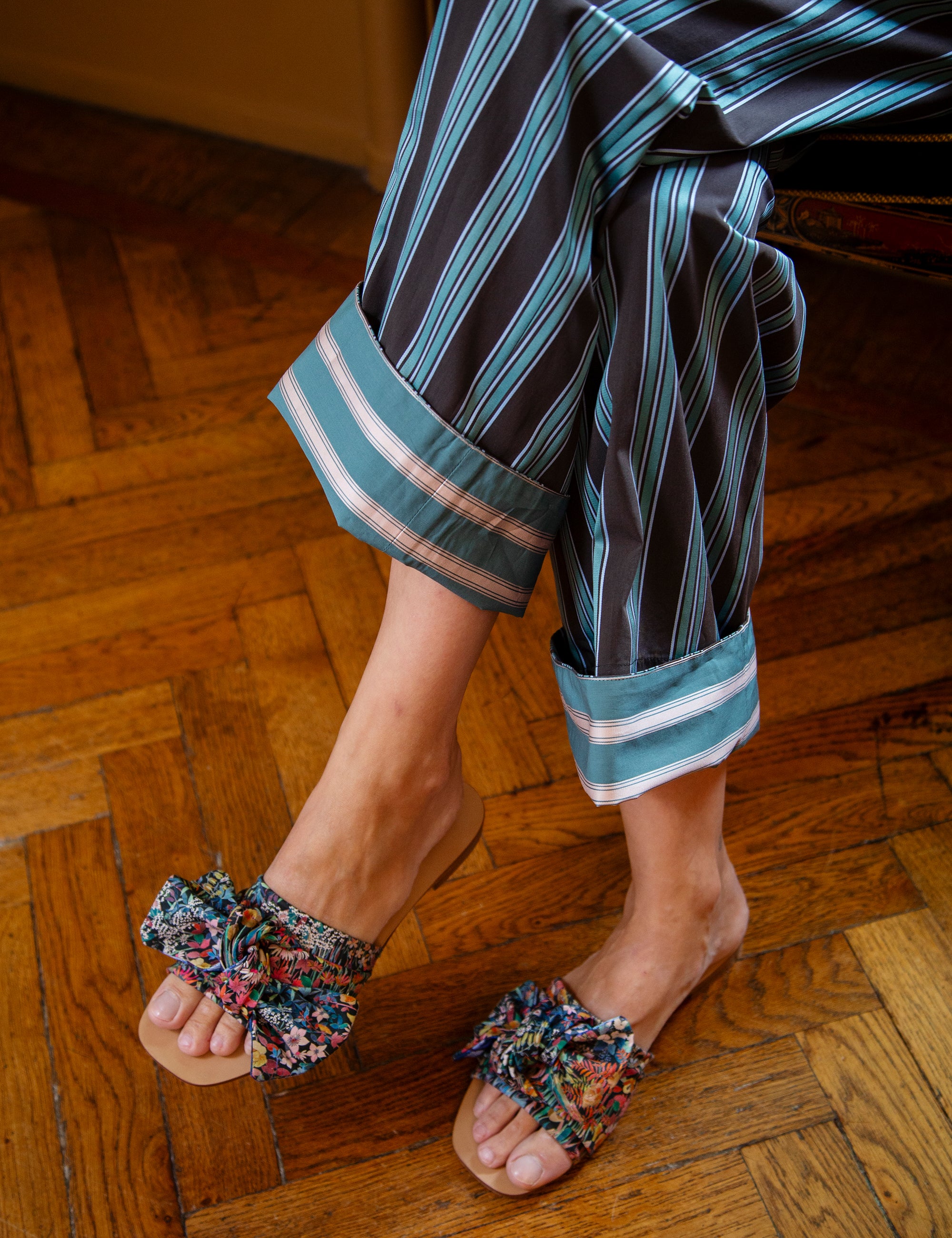 Woman wearing striped pants and colorful sandals on a wooden floor.