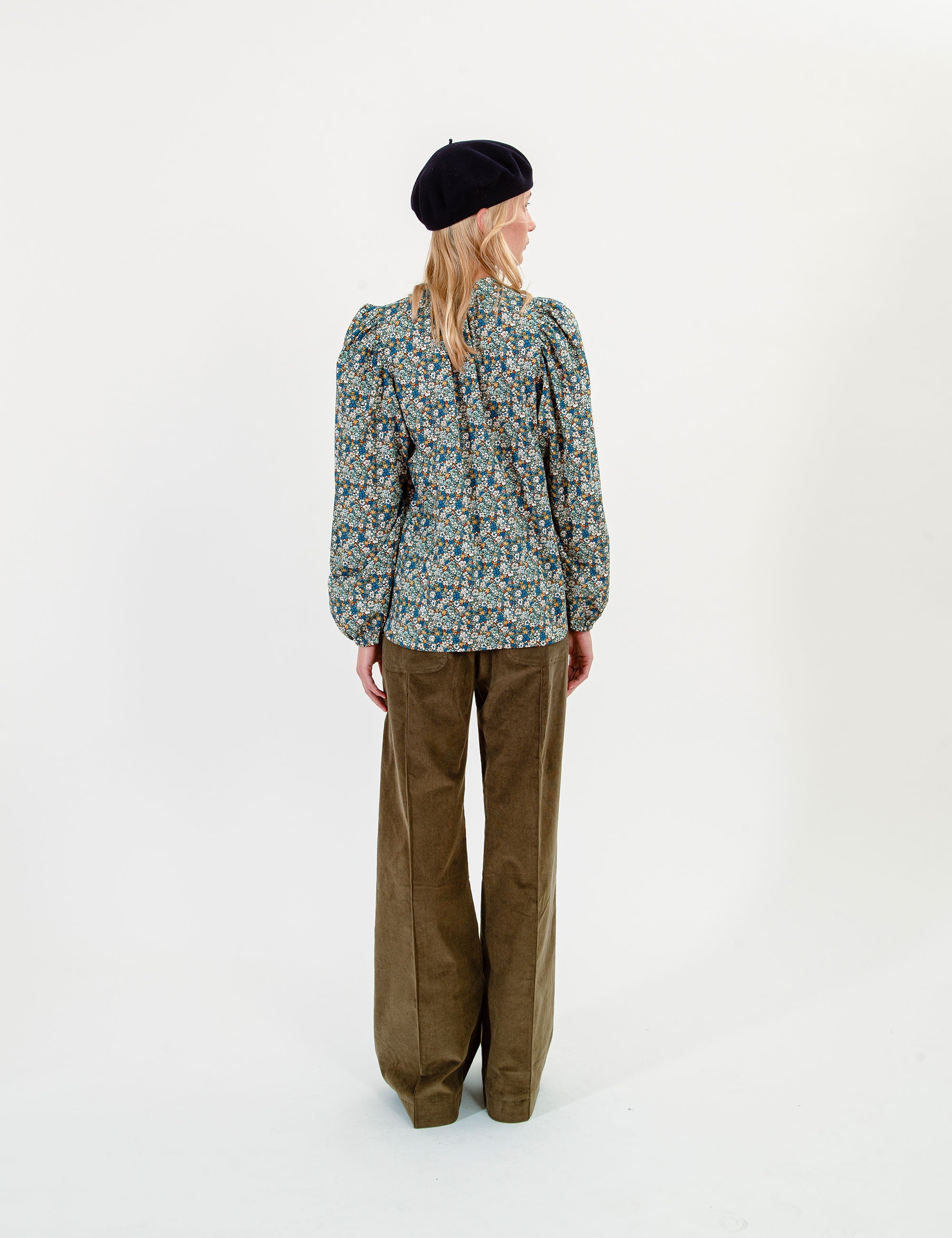 Woman wearing a patterned blouse and olive green pants on a white background