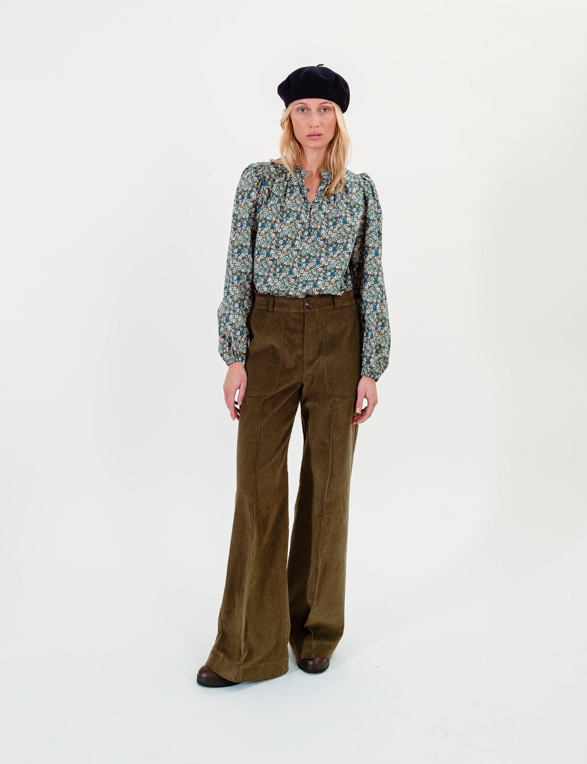Woman wearing a floral blouse, olive green pants and a dark beret