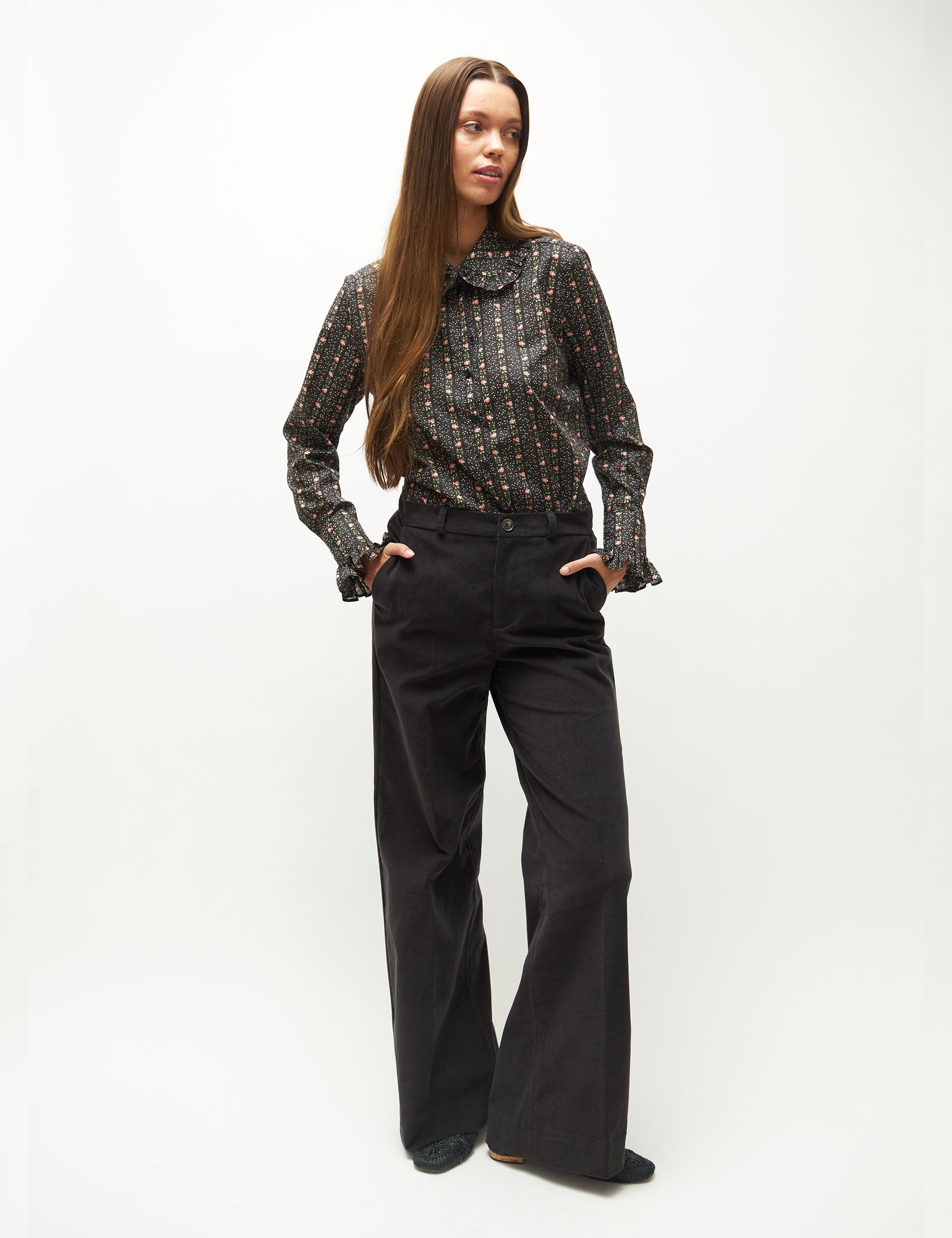 Woman wearing a patterned blouse and black pants on a white background