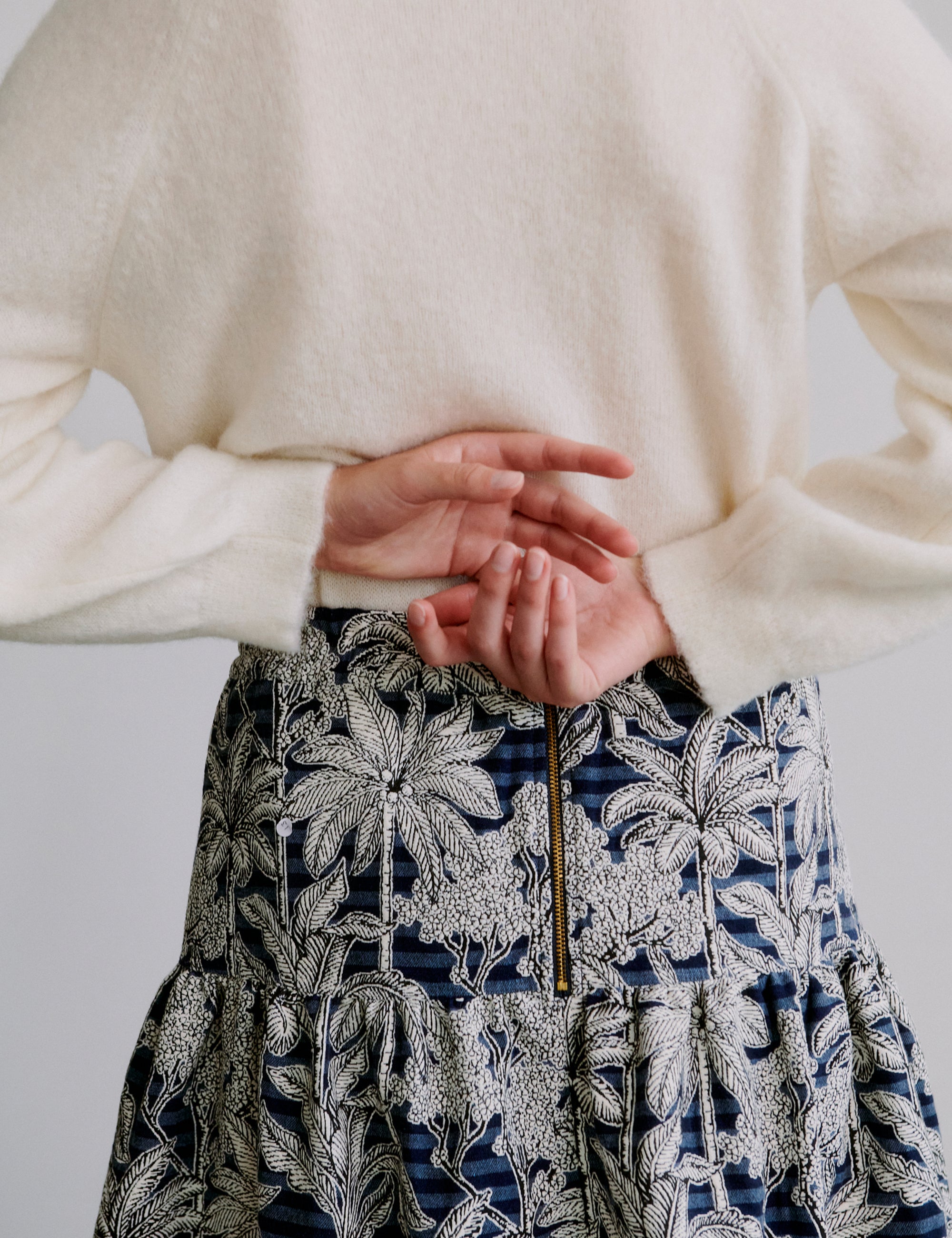 Person wearing a cream sweater and a patterned skirt with a white background