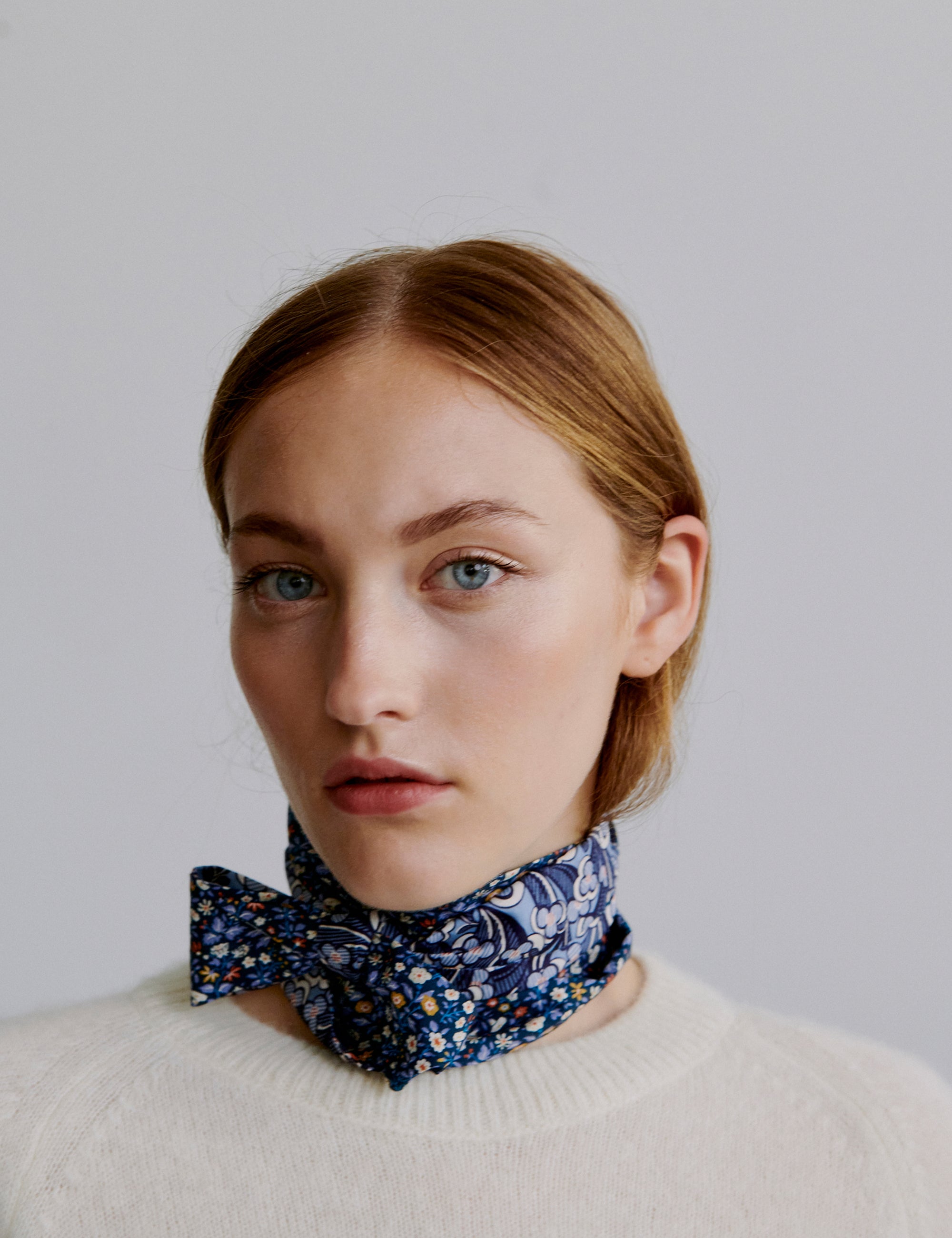Woman wearing a blue floral scarf around her neck against a plain background