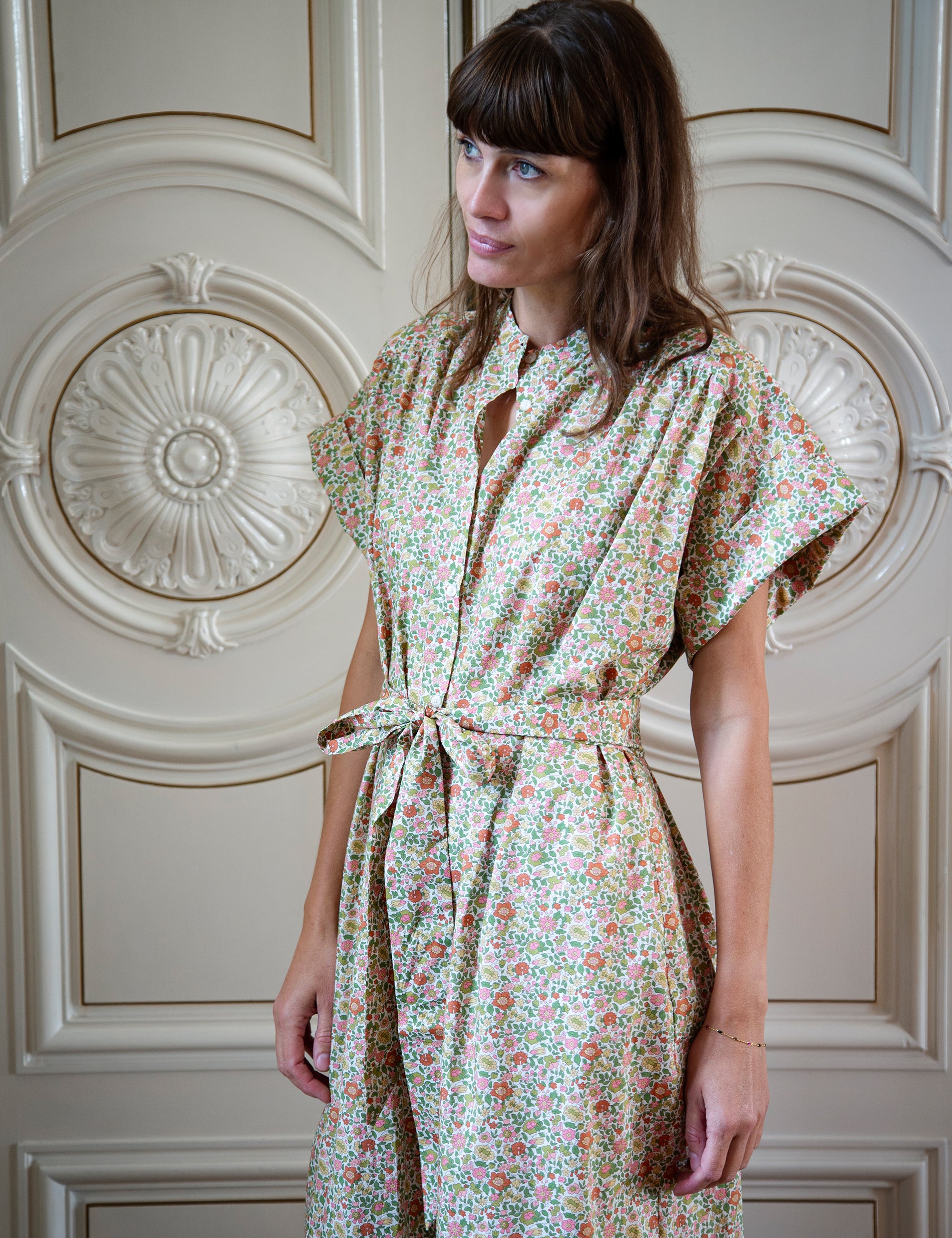 Woman wearing a floral dress standing in front of an ornate wall.