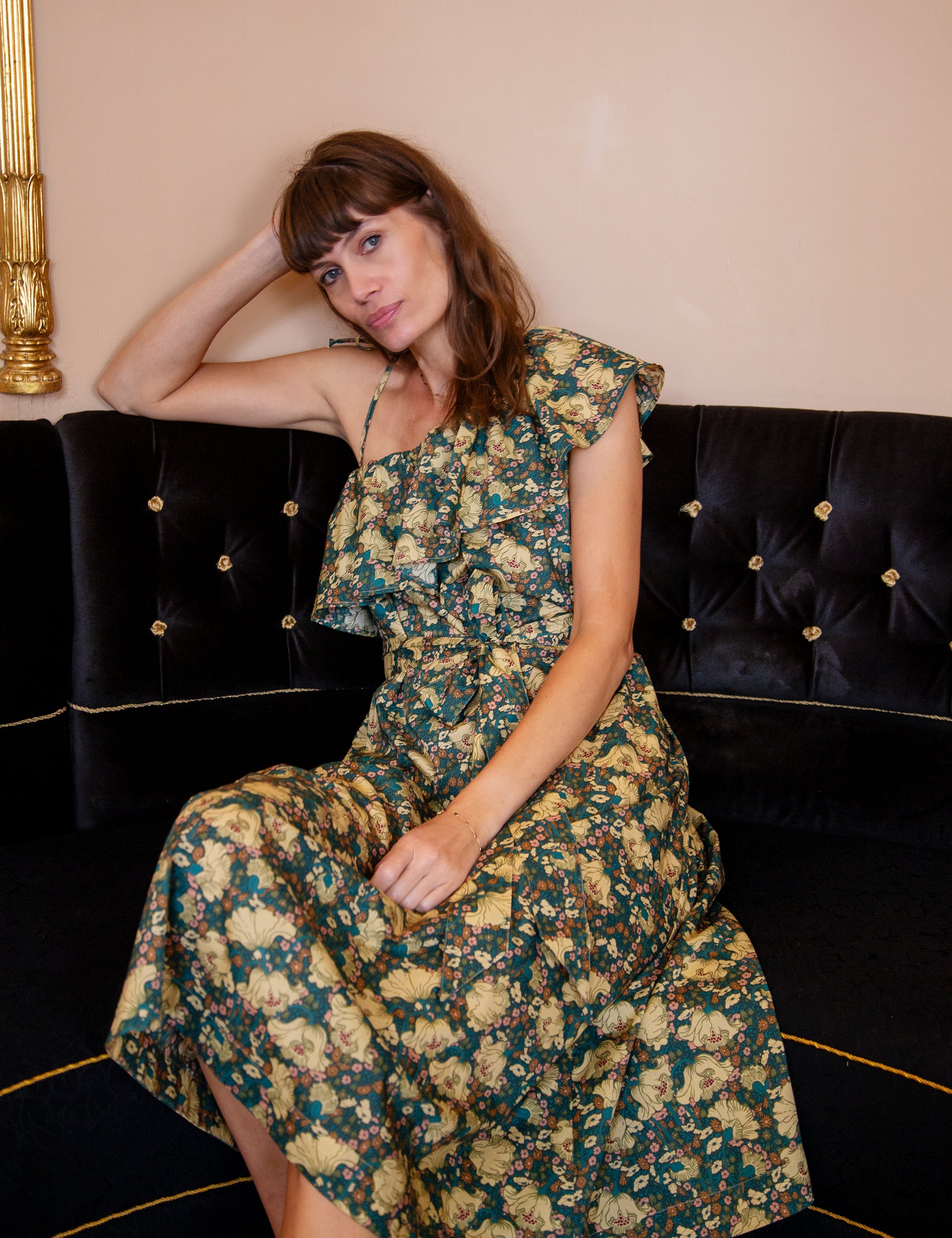 Woman in a floral dress sitting on a black couch with gold accents.