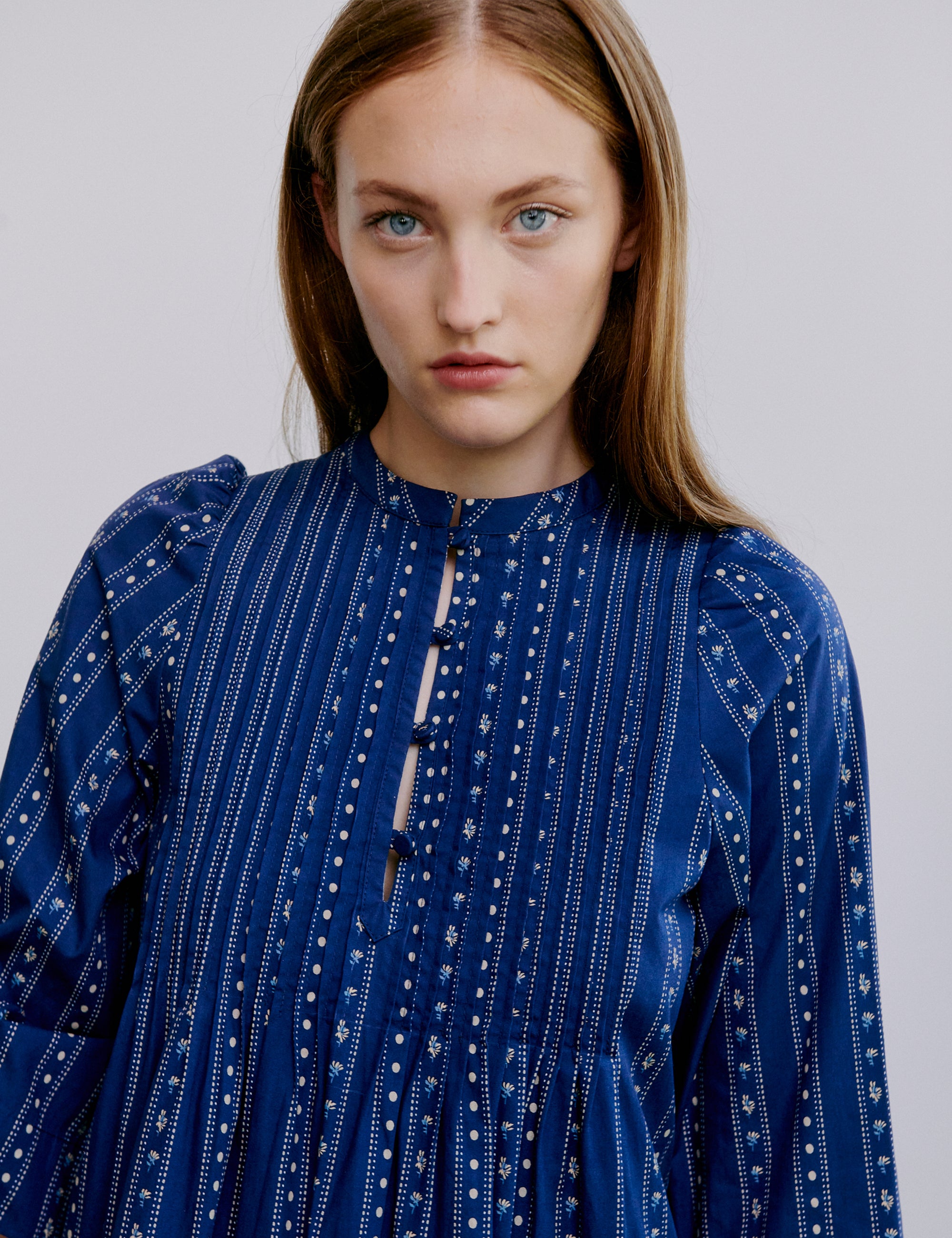 Woman wearing a blue patterned dress against a plain background