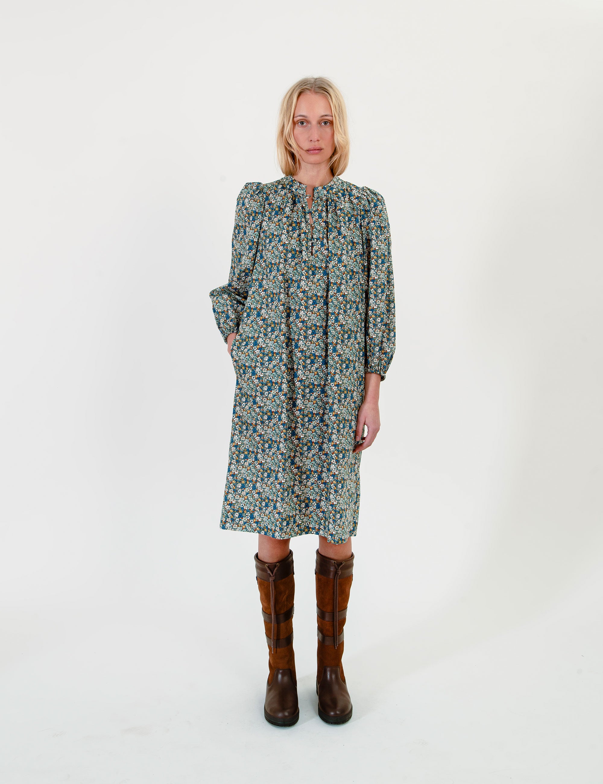Woman wearing a short green-blue floral dress with long sleeves and a belt on a white background