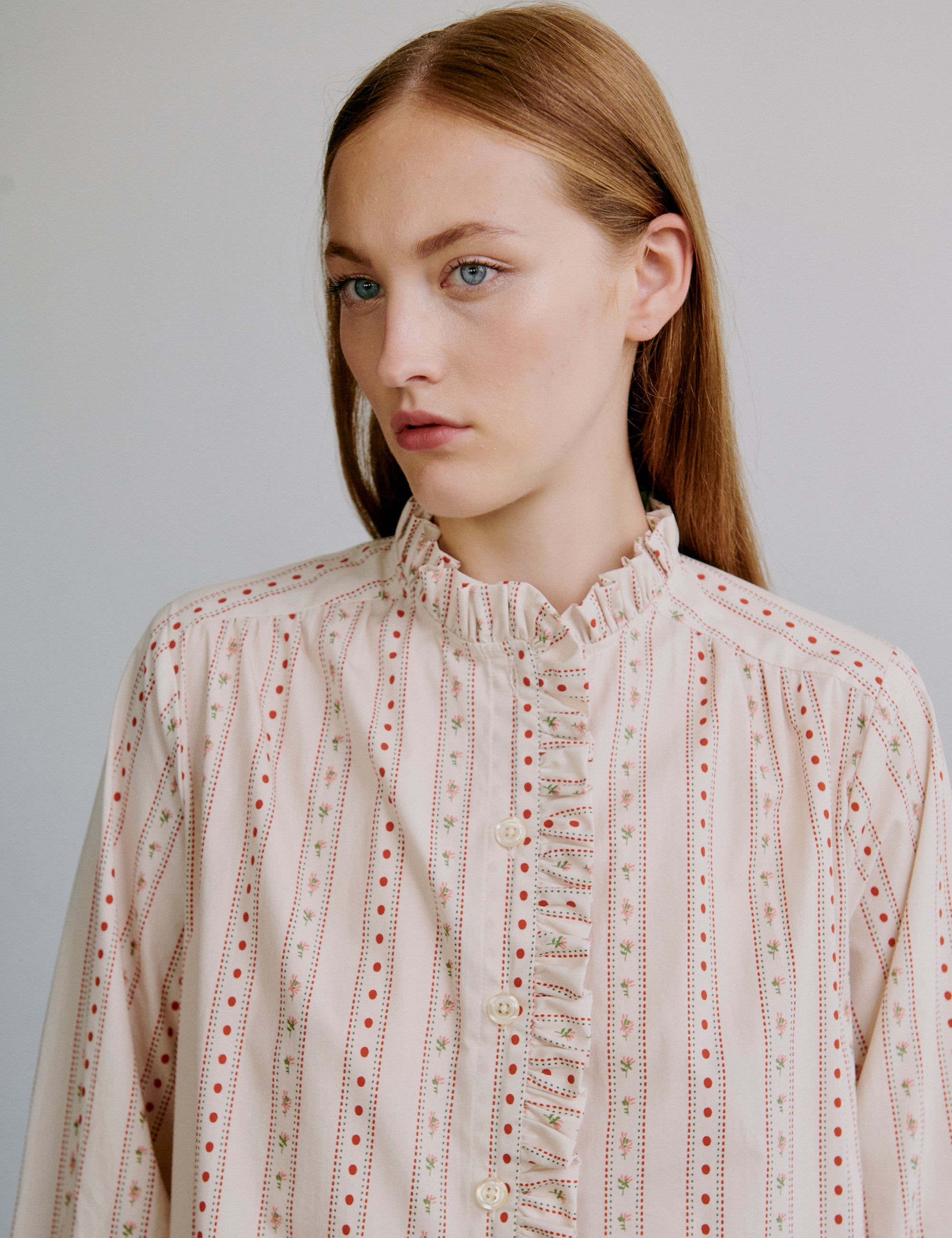 Woman wearing a light colored patterned dress with long sleeves and frills