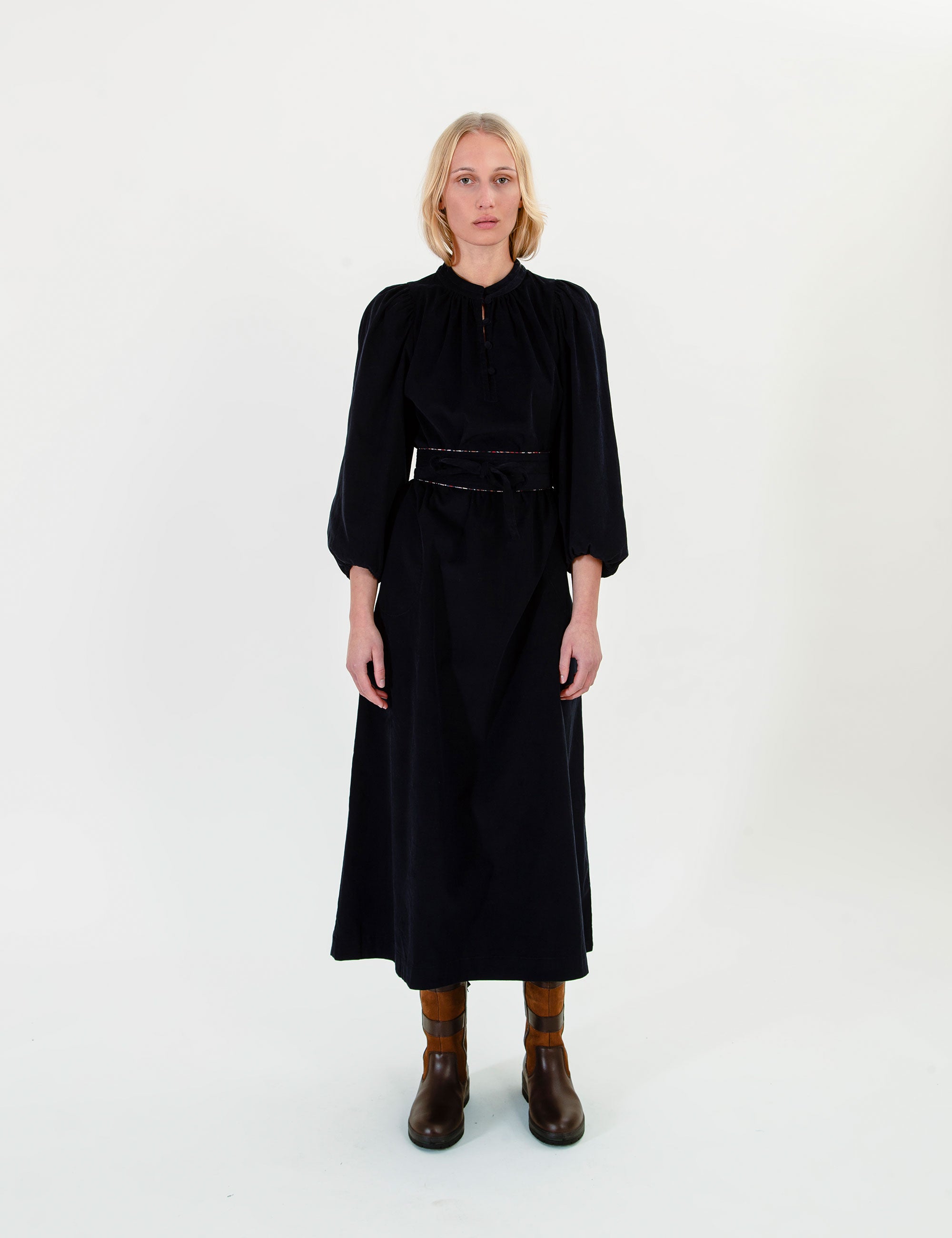 Woman wearing a dark blue corduroy dress with a belt on a white background