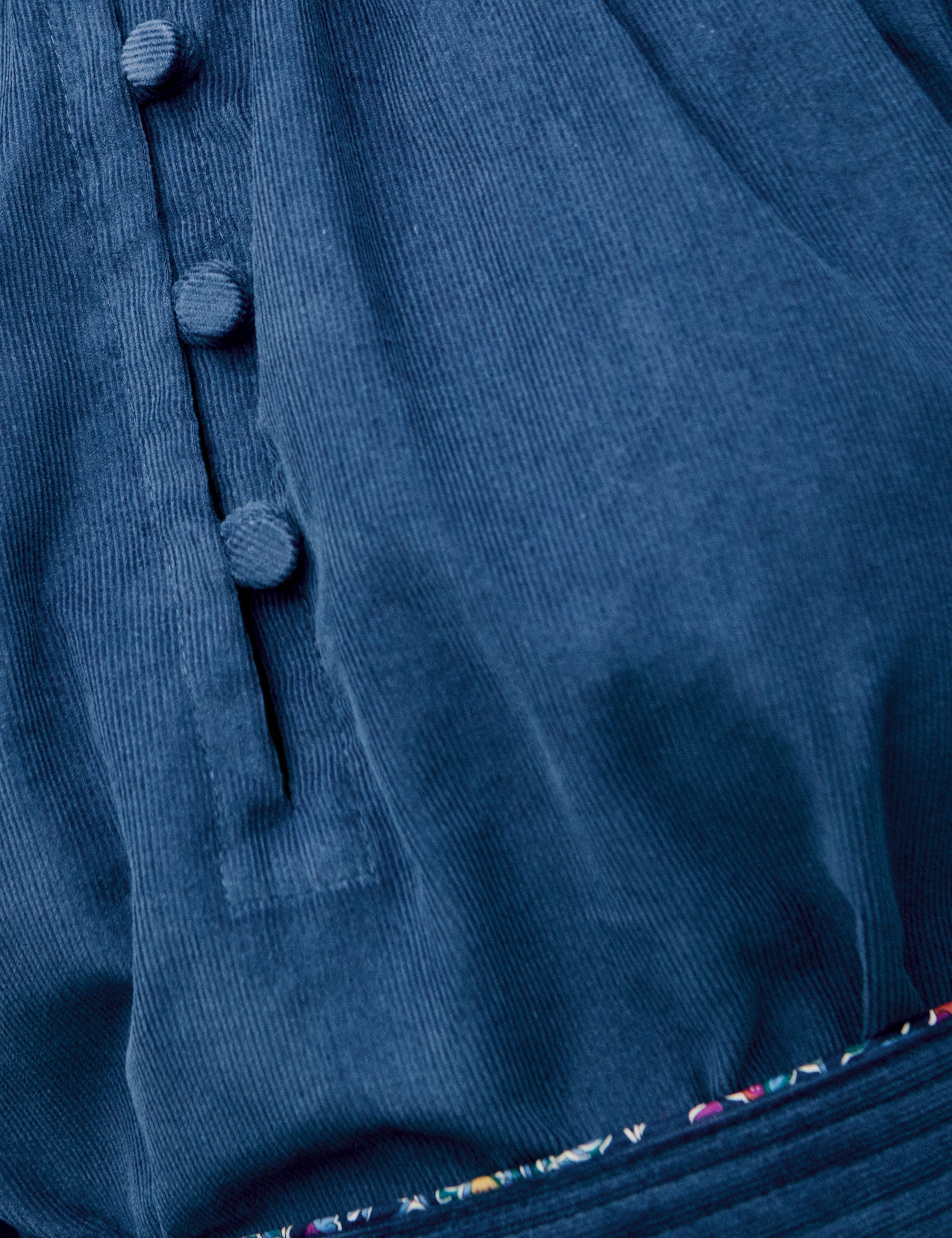 Detailed view of covered buttons and waist seam stitching on blue corduroy dress