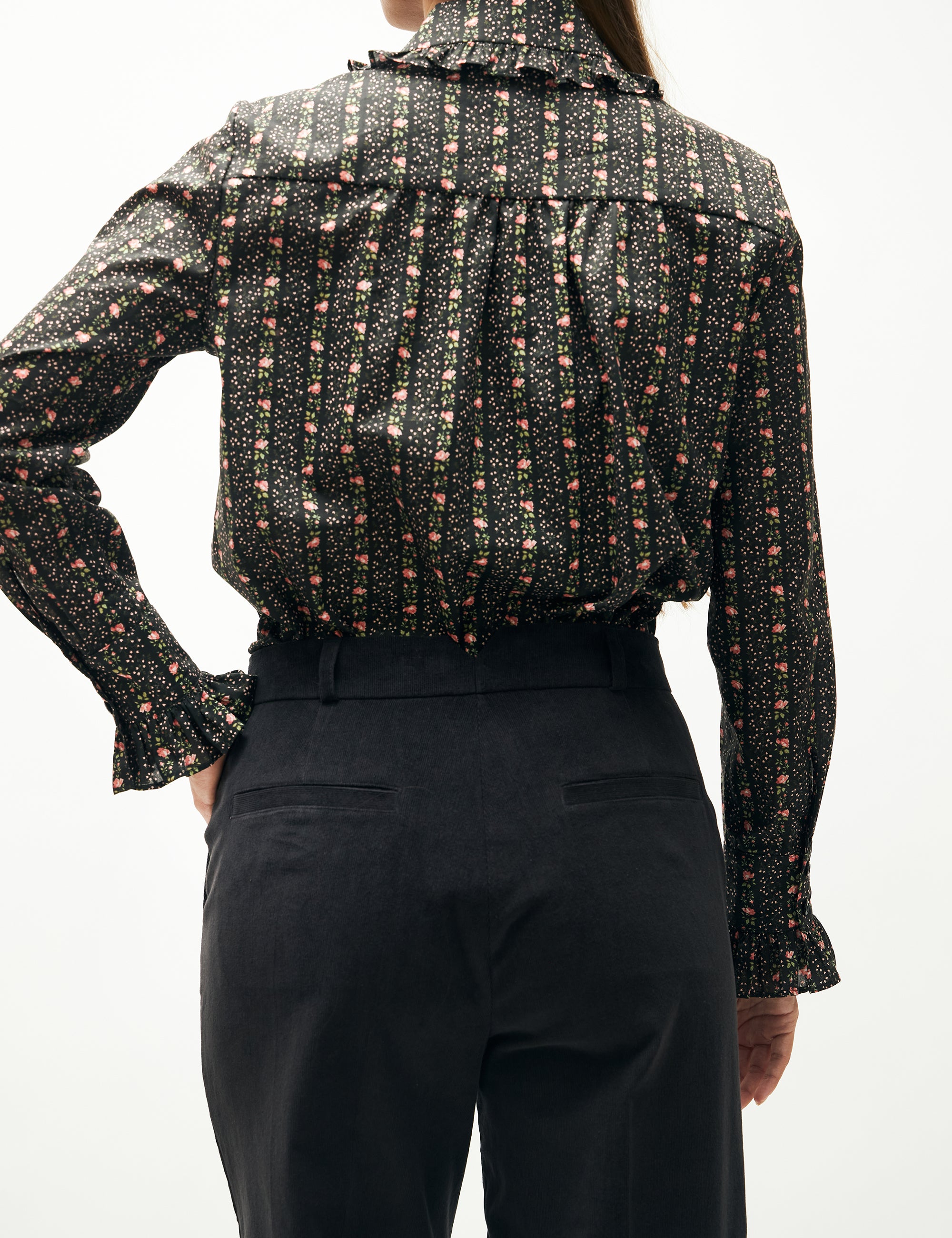 Kvinna i vida blå sammetsbyxor och blommig randig långärmad blus med krage