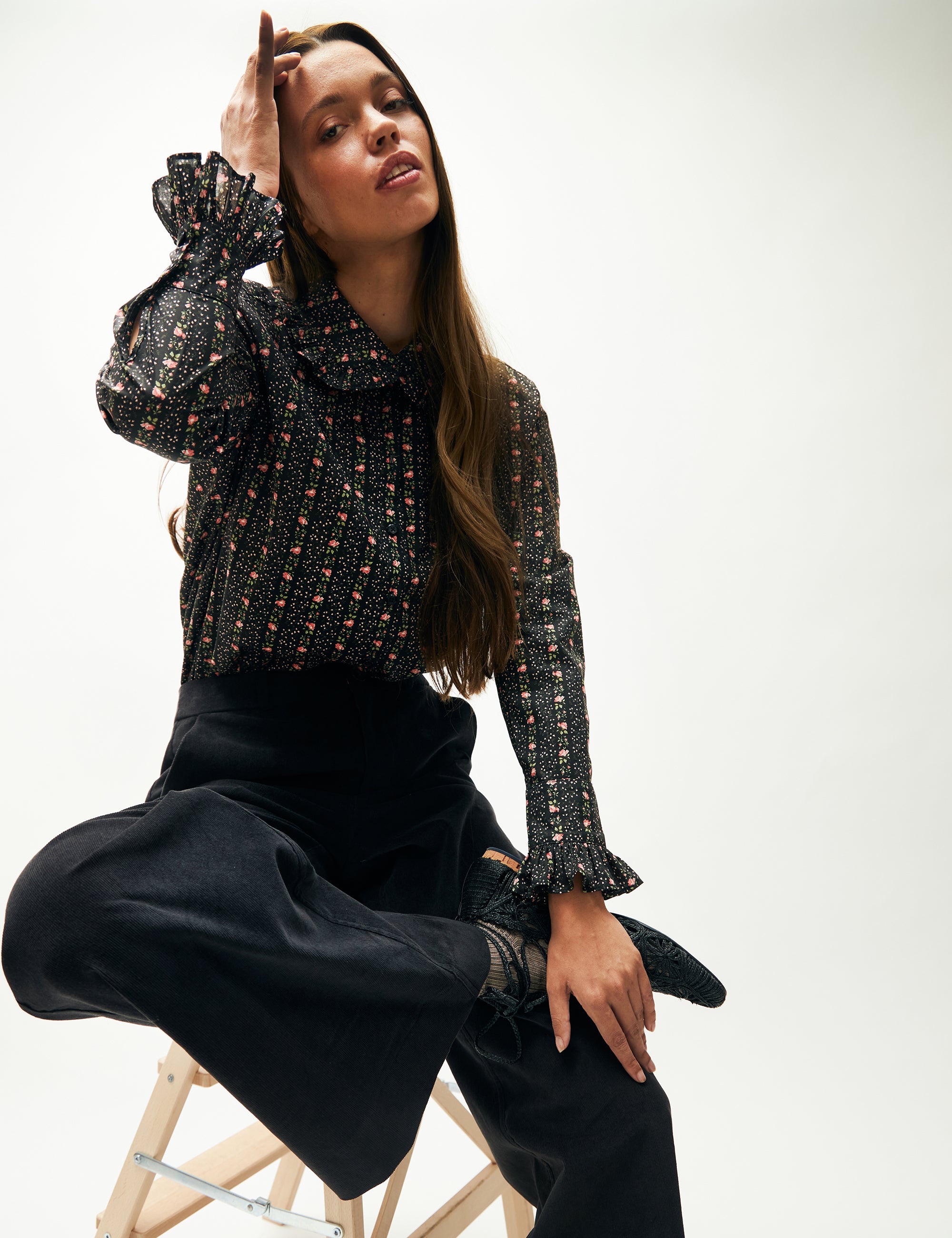 Kvinna i vida blå sammetsbyxor och blommig randig långärmad blus med krage