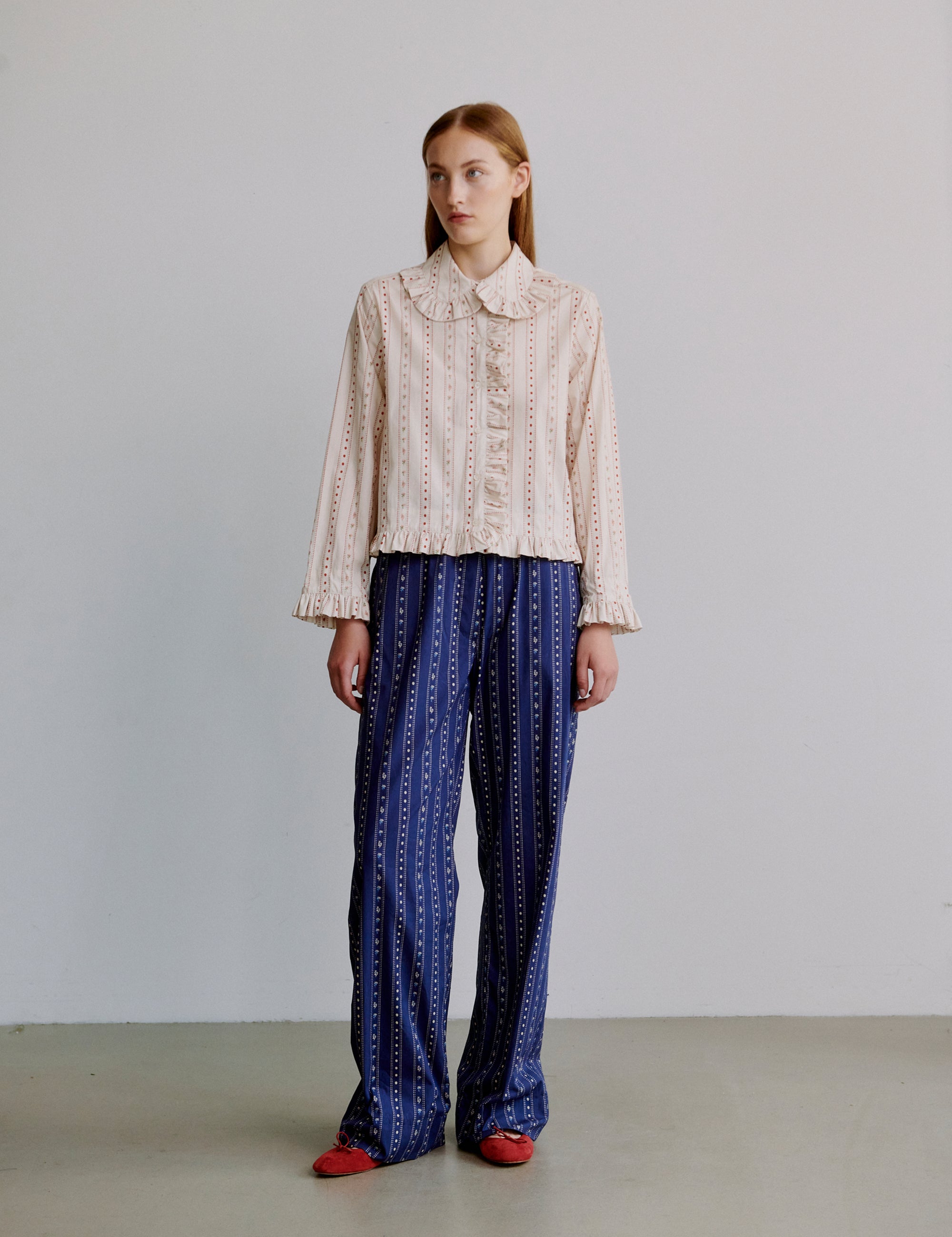 Woman wearing a white and pink floral patterned blouse and blue patterned pants against a plain background