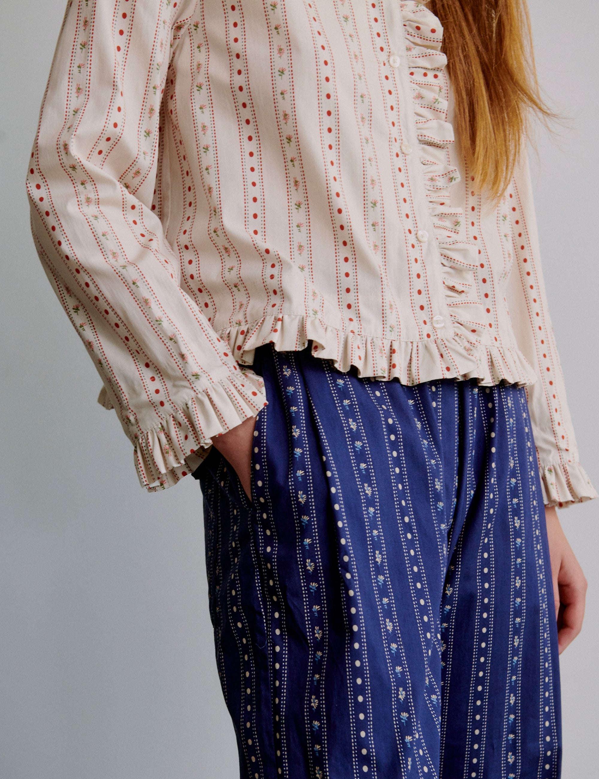 Woman wearing a patterned blouse and blue striped pants on a plain background