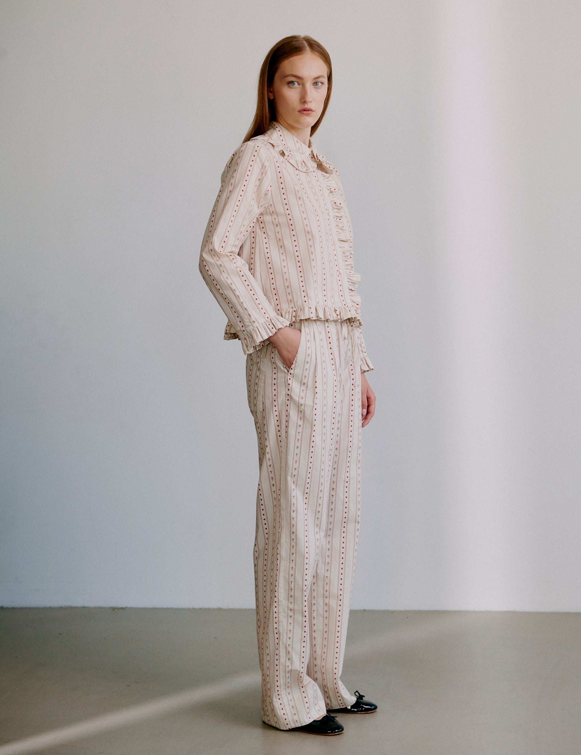 Woman wearing a matching top and pants set in beige with light pink pattern and frilled details