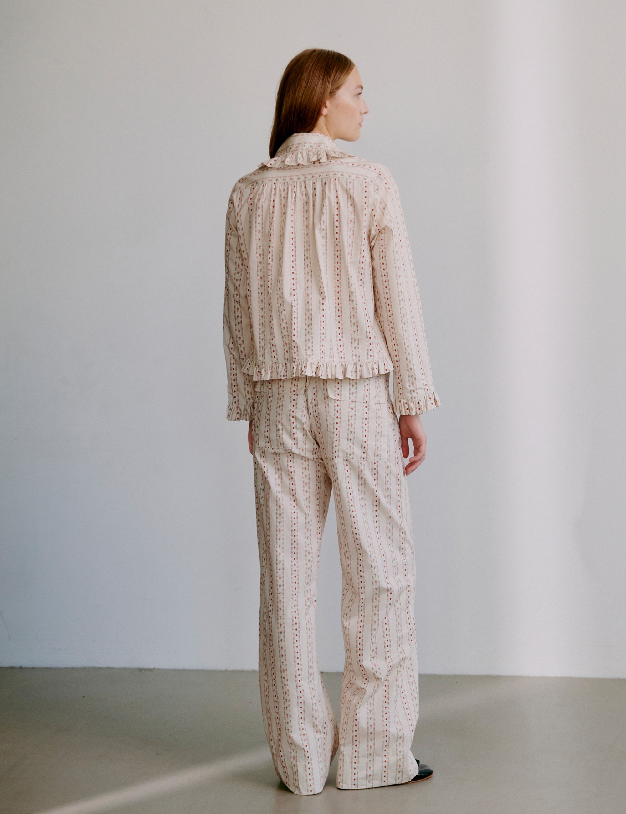 Woman wearing a matching top and pants set in beige with light pink pattern and frilled details