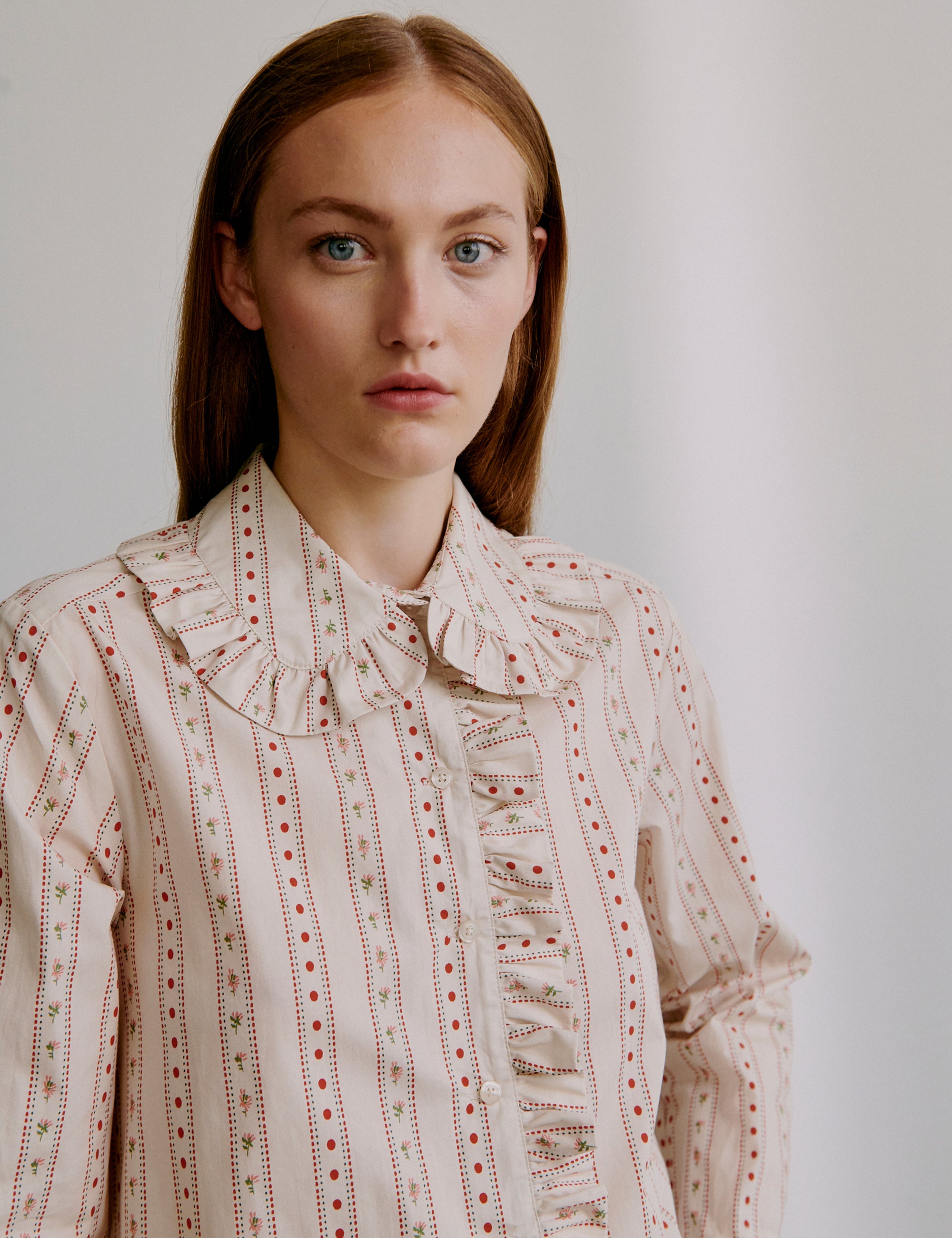 Woman wearing a beige and red patterned blouse with frilled details