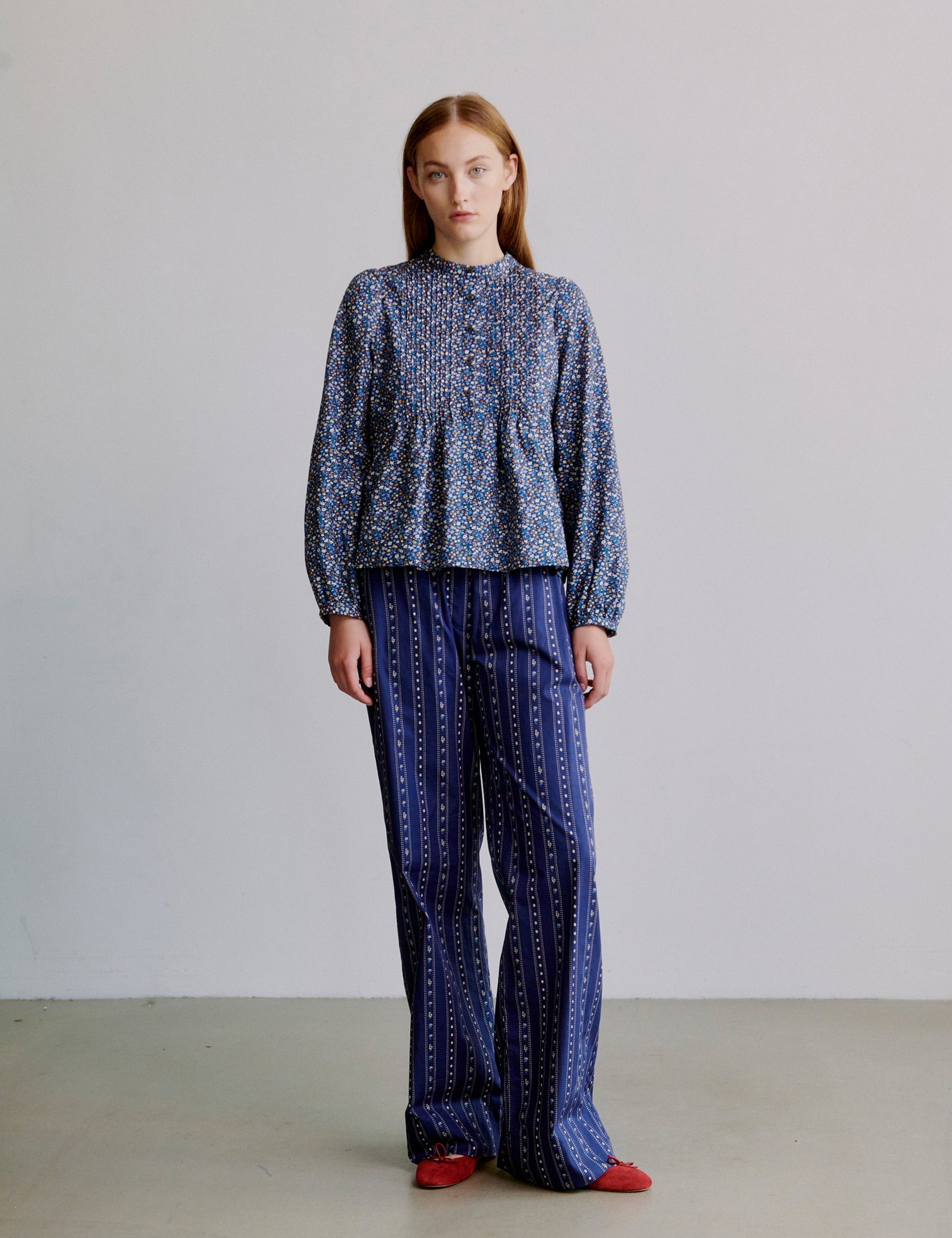 Woman wearing a blue floral patterned long sleeve shirt and blue striped pants against a plain background