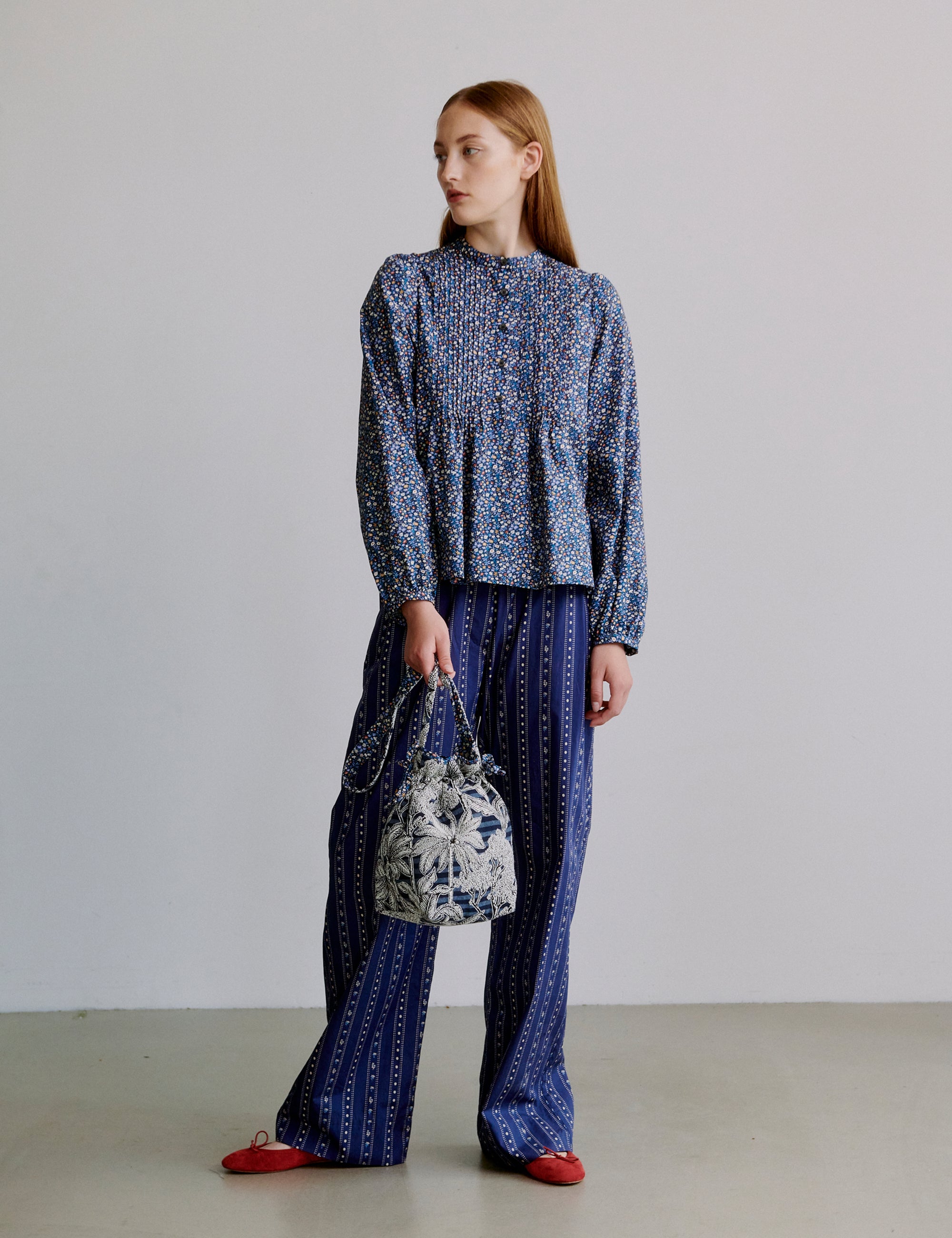 Woman wearing a blue floral patterned outfit holding a matching blue handbag against a plain background