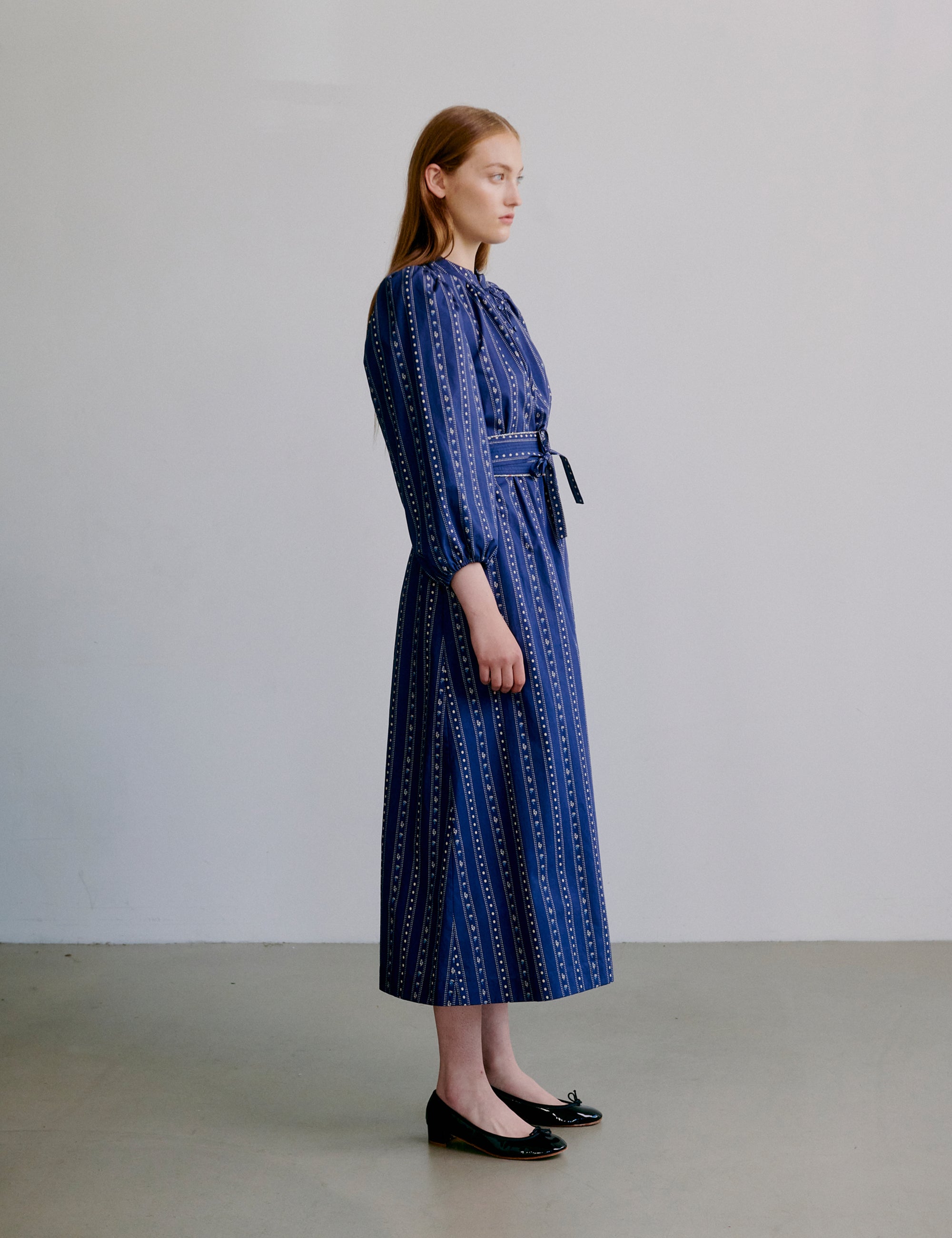 Woman wearing a blue patterned dress with long puff sleeves, collar buttons and matching belt