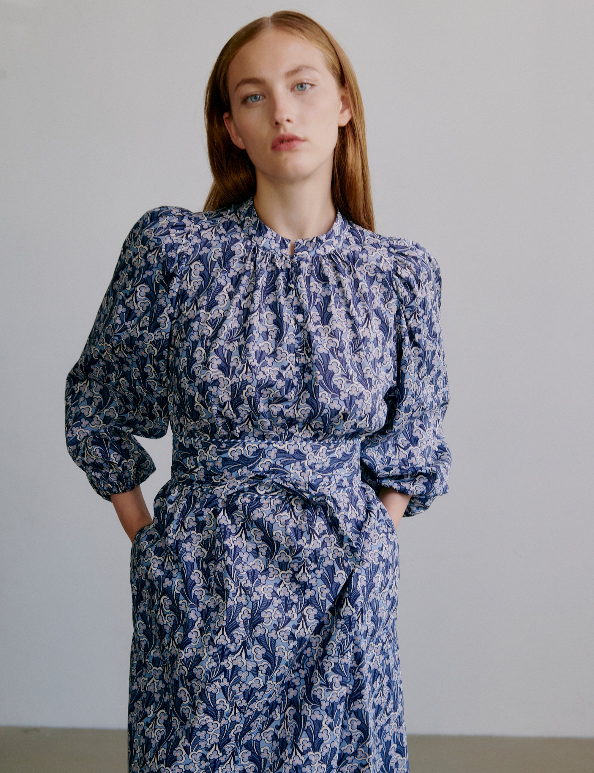Woman wearing a blue floral dress with long sleeves, buttons at the front and matching belt