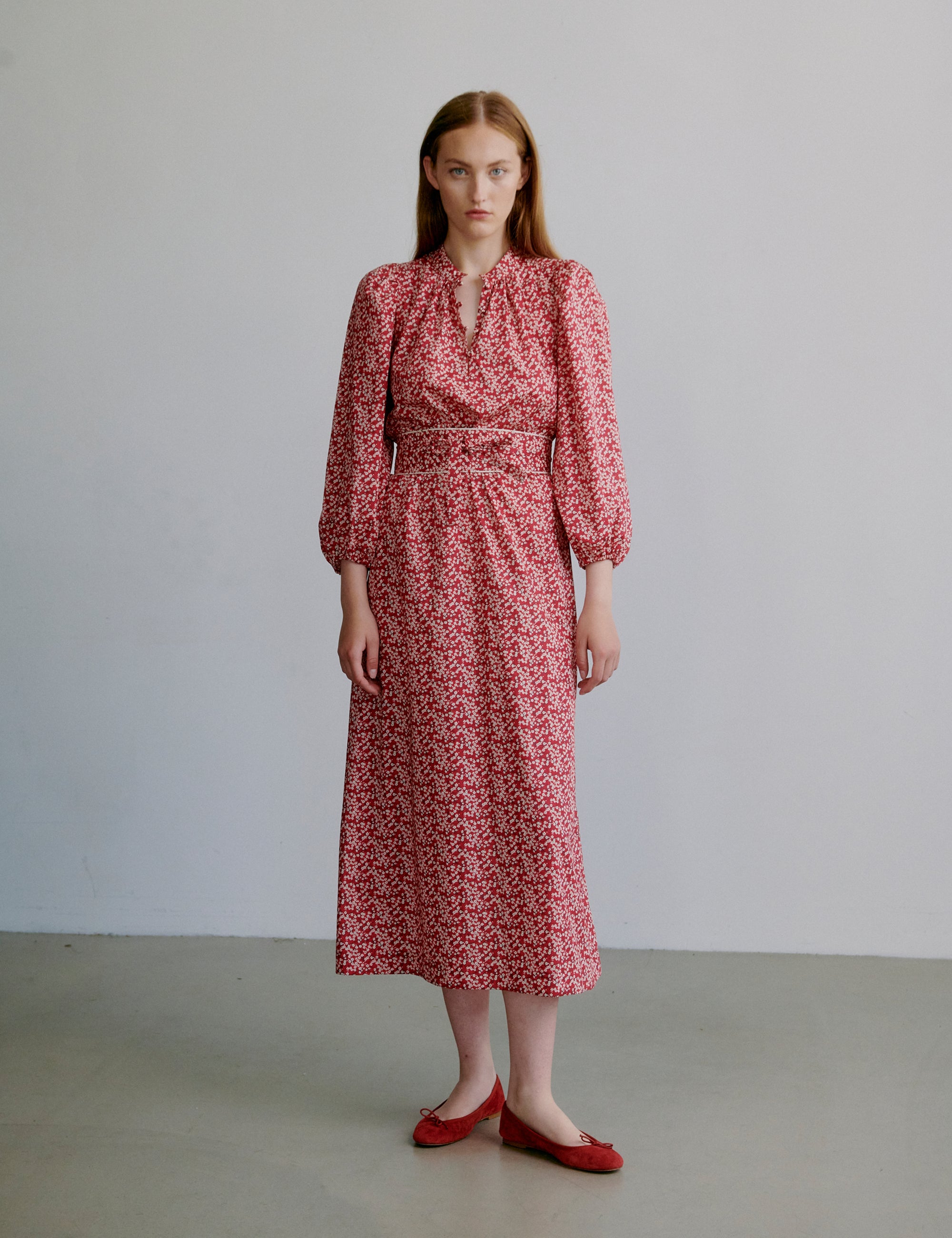 Woman wearing a red floral dress with long puff sleeves, round collar with covered buttons and matching fabric belt