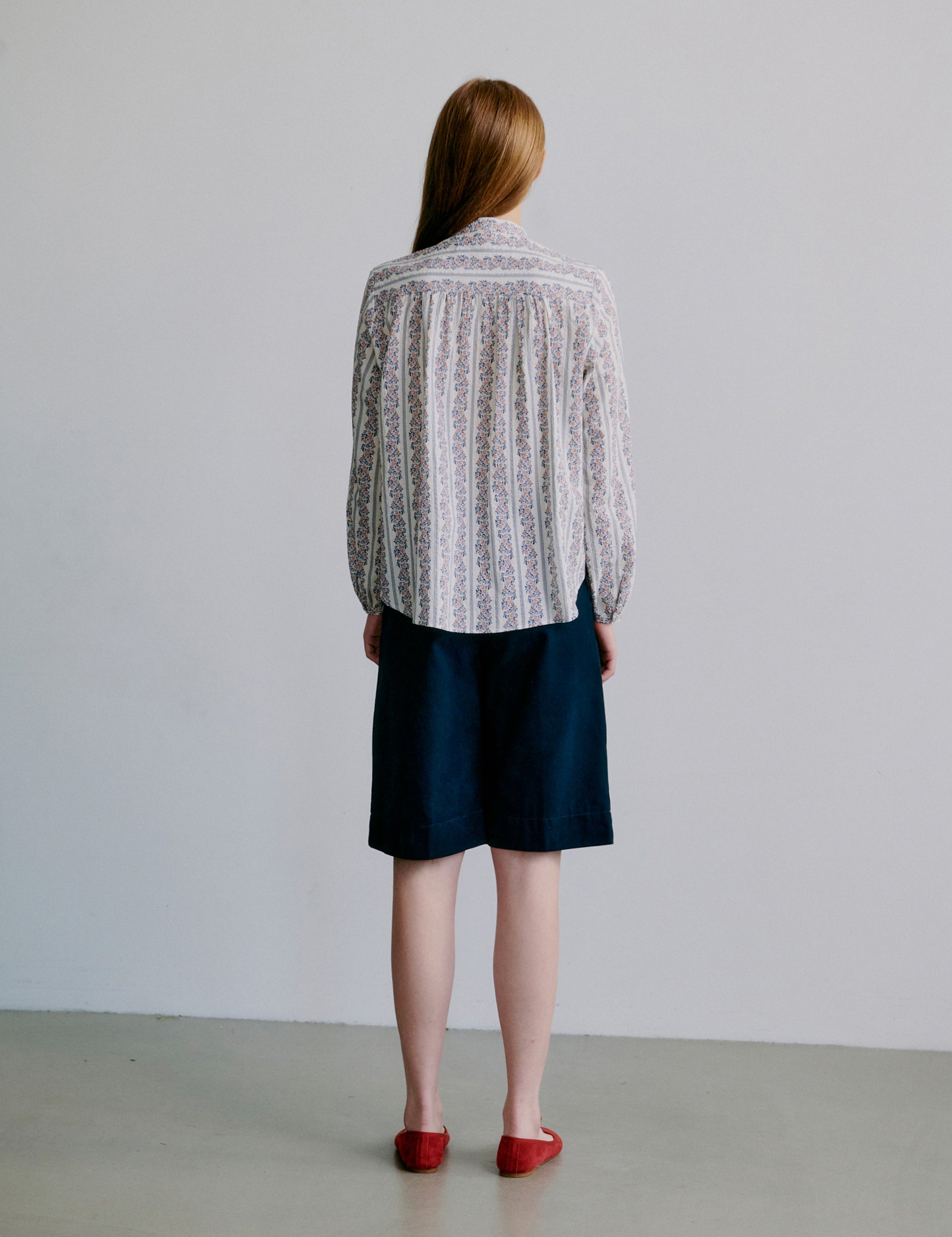 Woman wearing a long sleeve floral patterned blouse and navy shorts