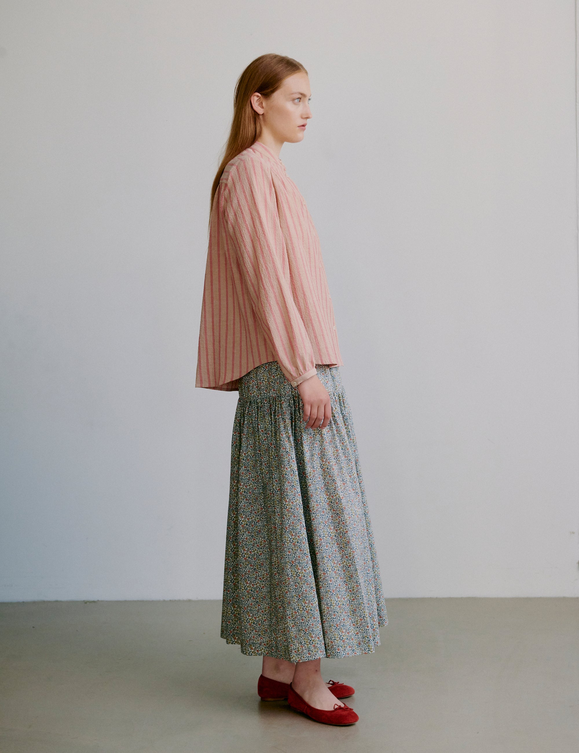 Woman wearing a pink striped long sleeve shirt and flower patterned skirt against a plain background
