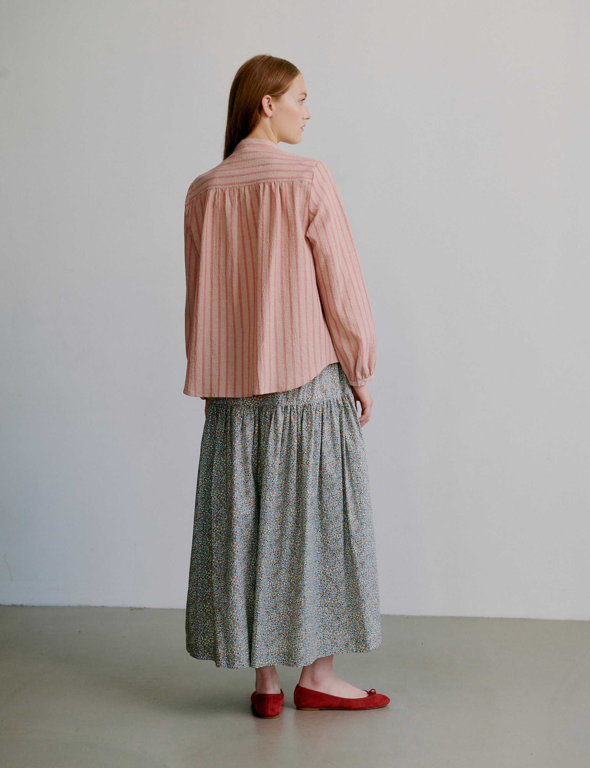 Woman wearing a pink striped long sleeve shirt and flower patterned skirt against a plain background