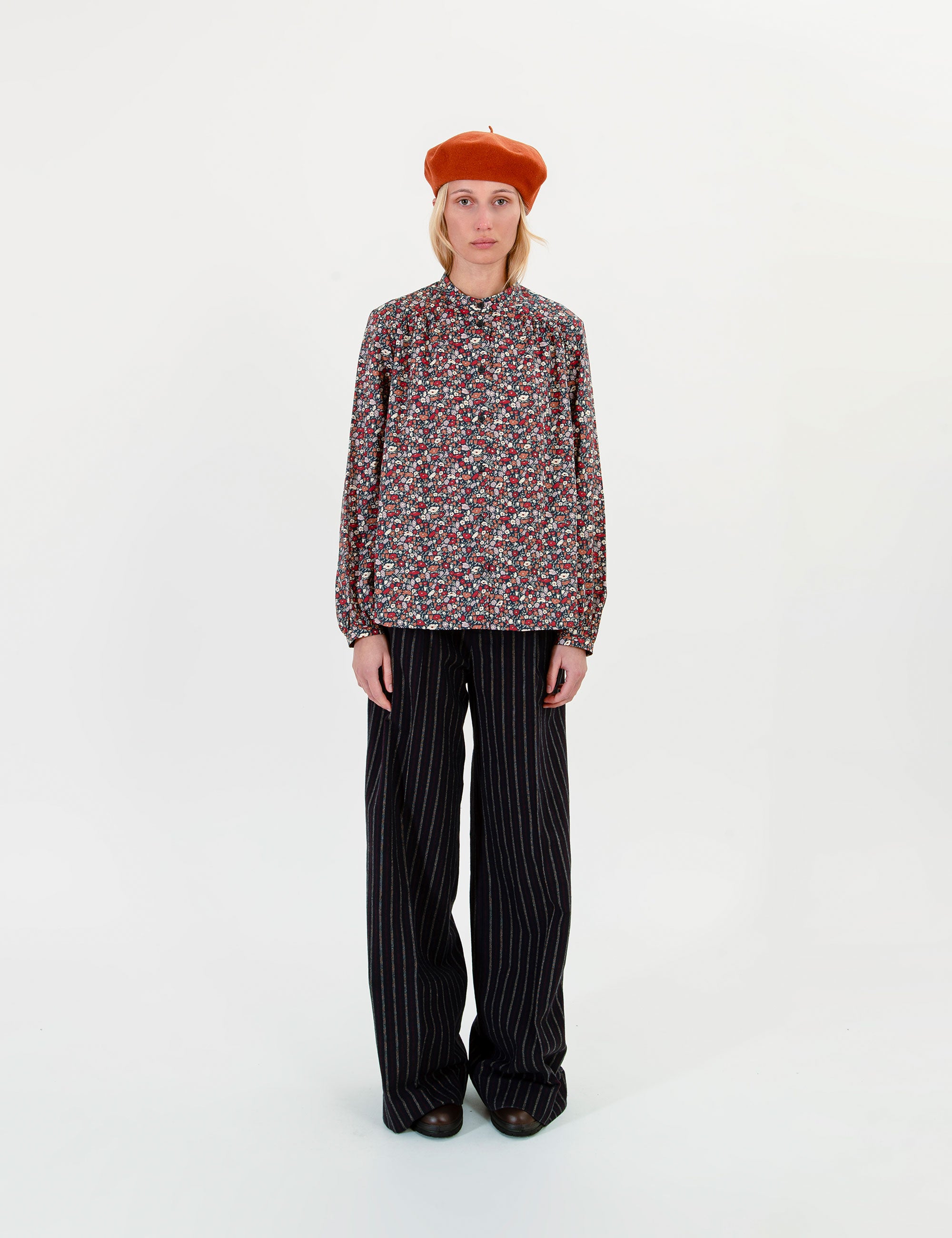 Woman wearing a flower patterned blouse and black striped pants with a orange beret