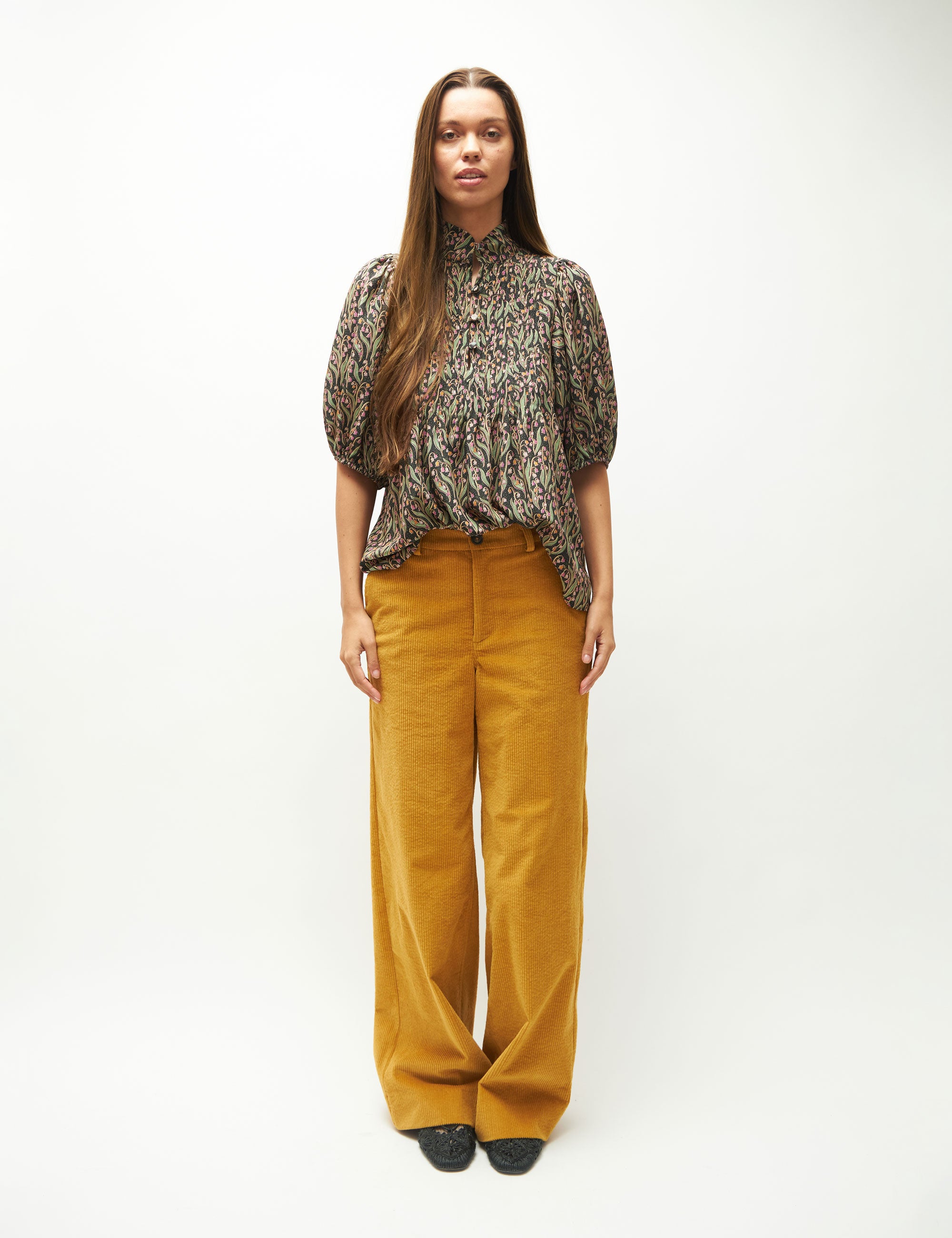 Woman wearing a patterned blouse and mustard yellow pants on a white background
