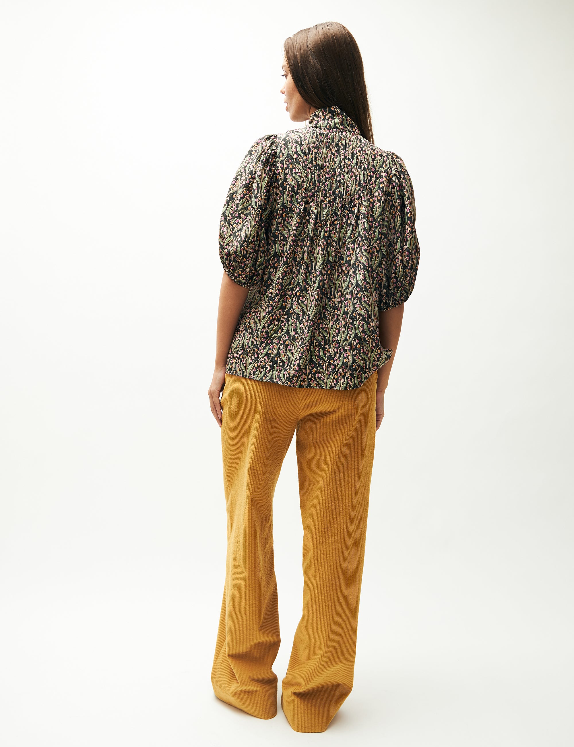 Woman in wide yellow corduroy pants and pink and green flower patterned blouse with short sleeves