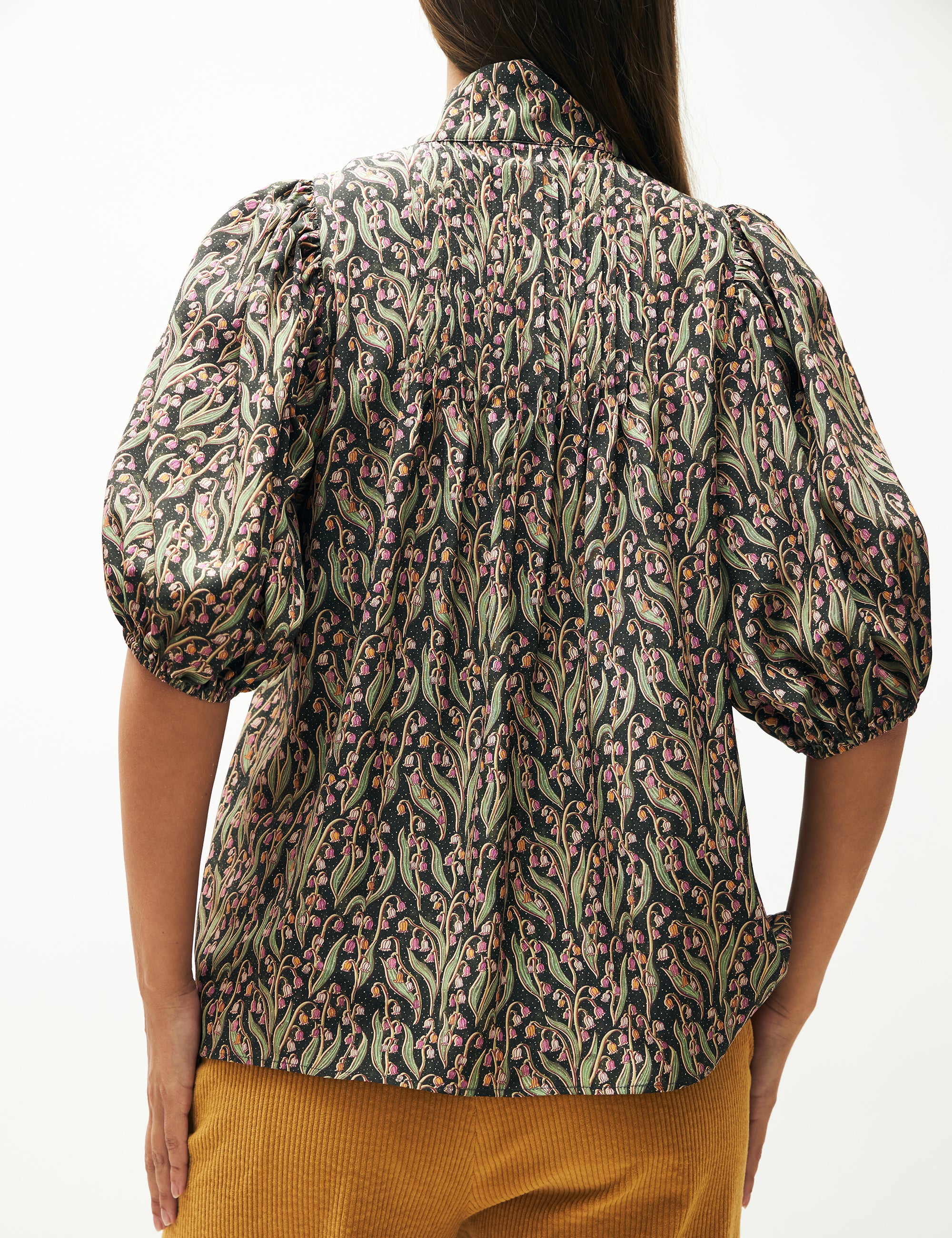 Woman in wide yellow corduroy pants and pink and green flower patterned blouse with short sleeves