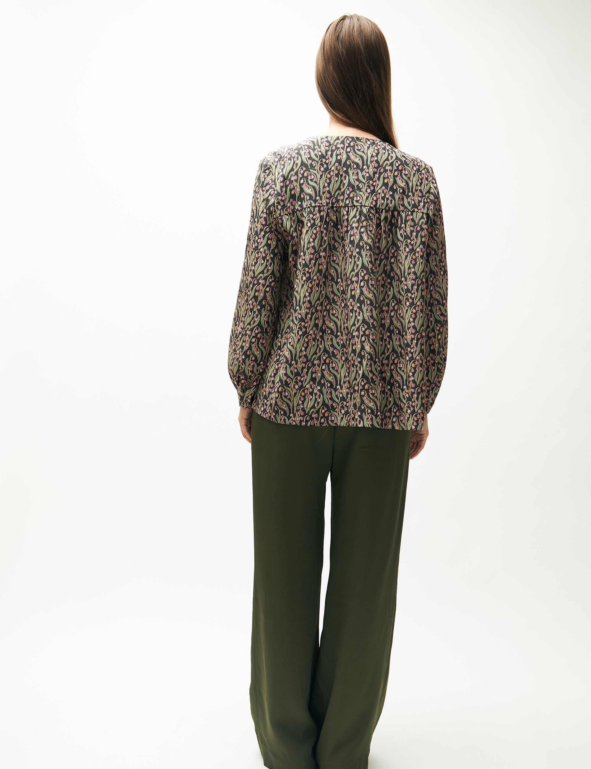 Woman in green pants and green and pink flower patterned shirt with long sleeves
