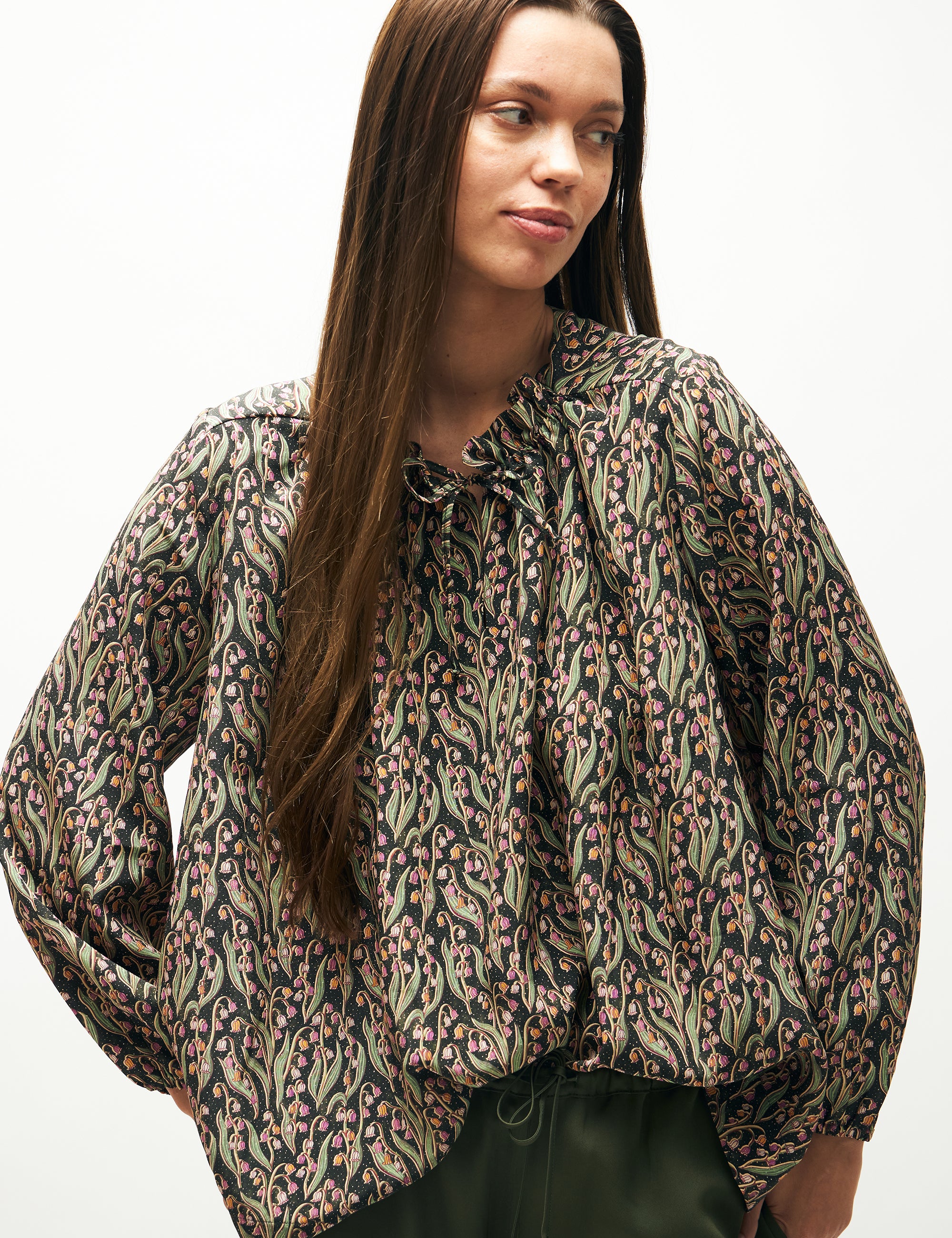 Woman in green pants and green and pink flower patterned shirt with long sleeves