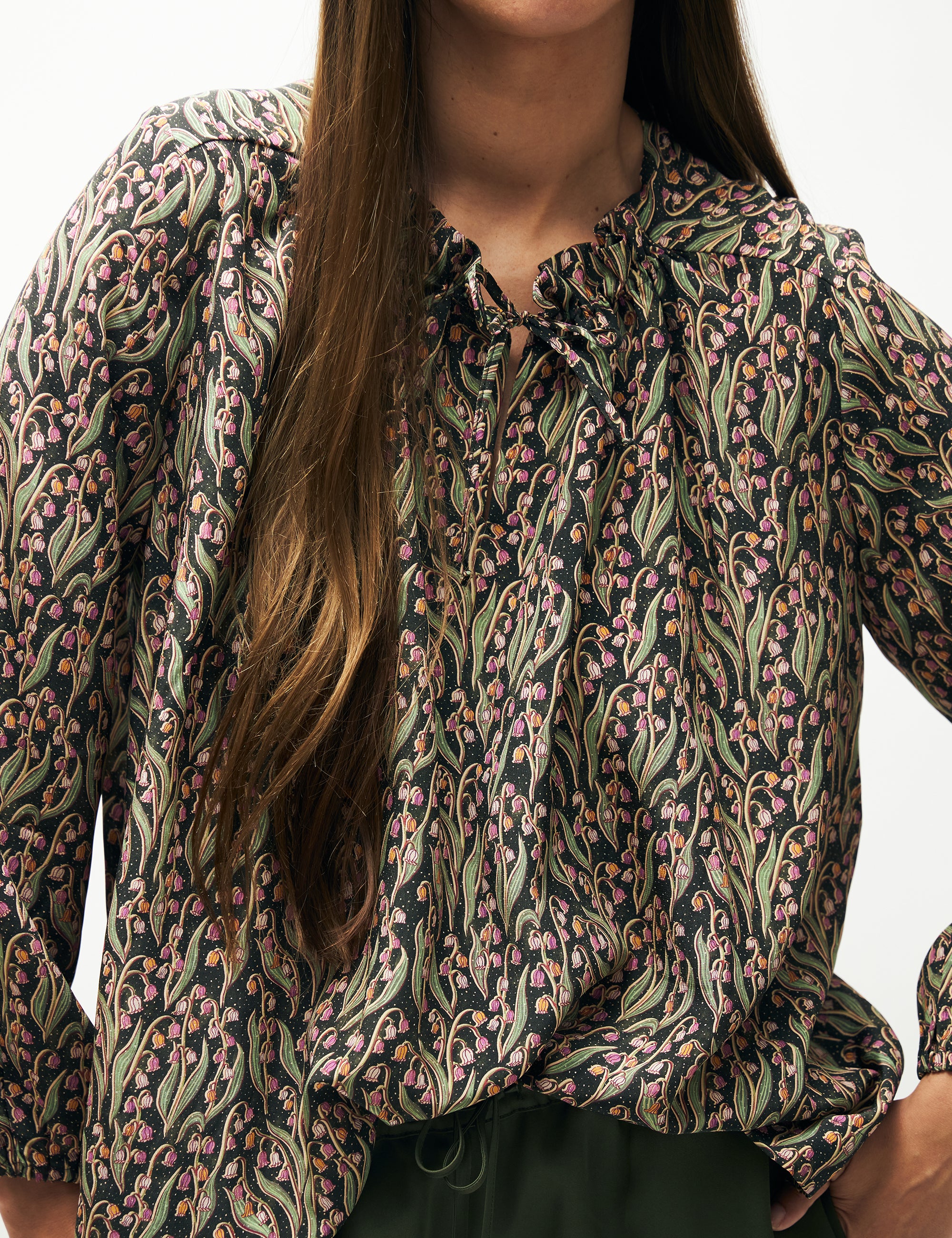 Woman in green pants and green and pink flower patterned shirt with long sleeves