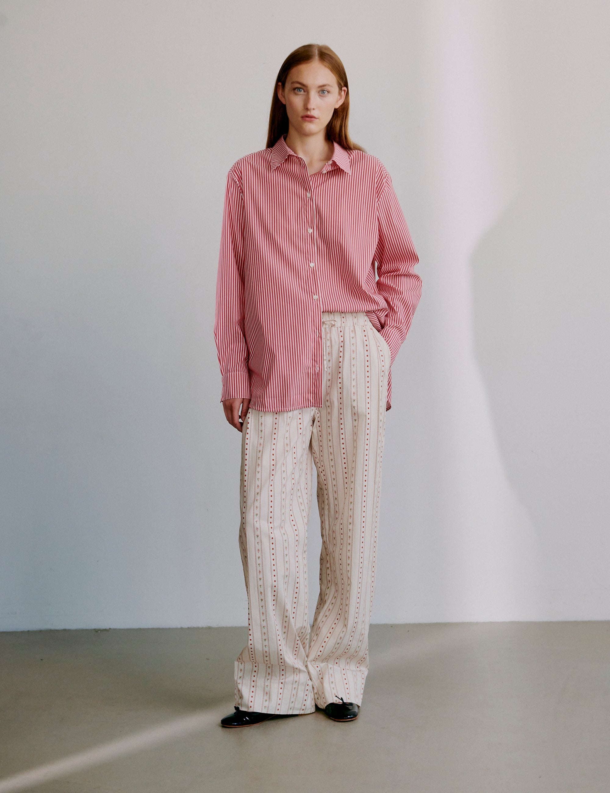 Woman wearing a red striped long sleeve shirt and beige patterned pants against a plain background