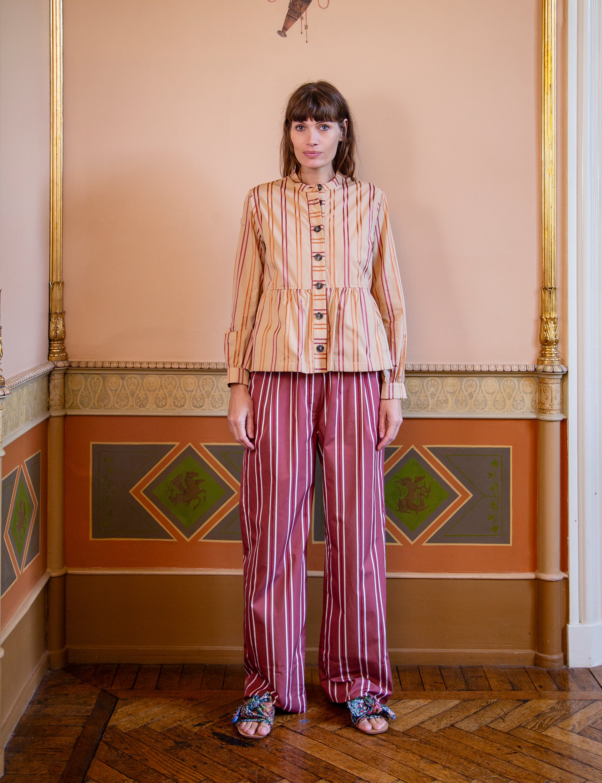 Woman wearing a striped outfit in an ornate room with decorative walls.