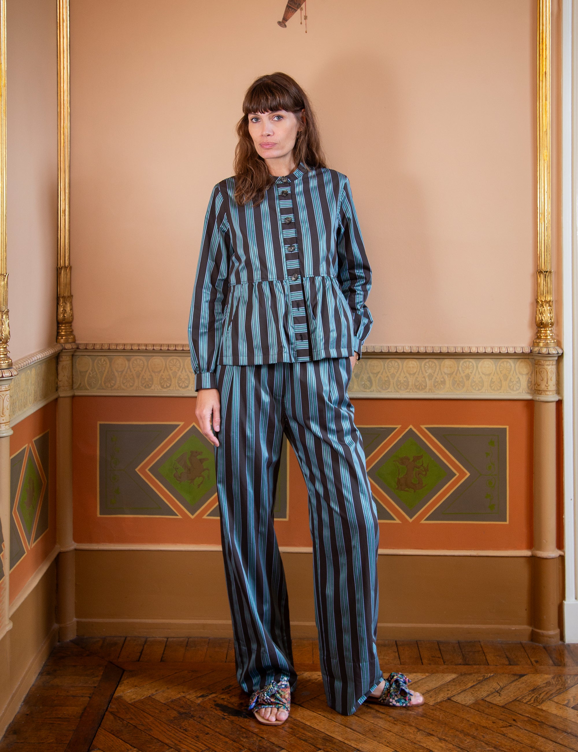 Woman wearing a green and black striped outfit standing in an ornate room with decorative walls.