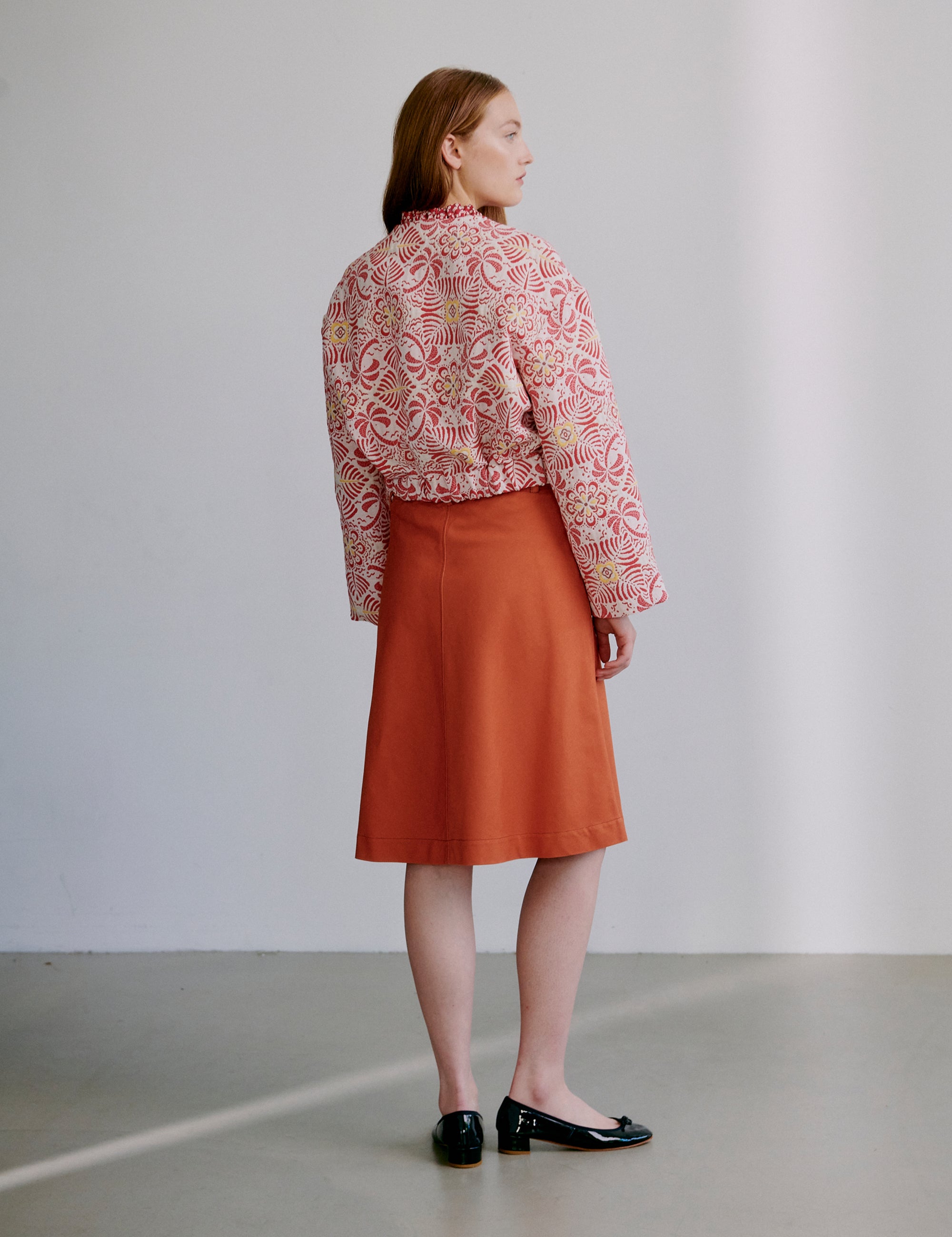 Woman wearing a red patterned jacket and orange skirt against a plain background