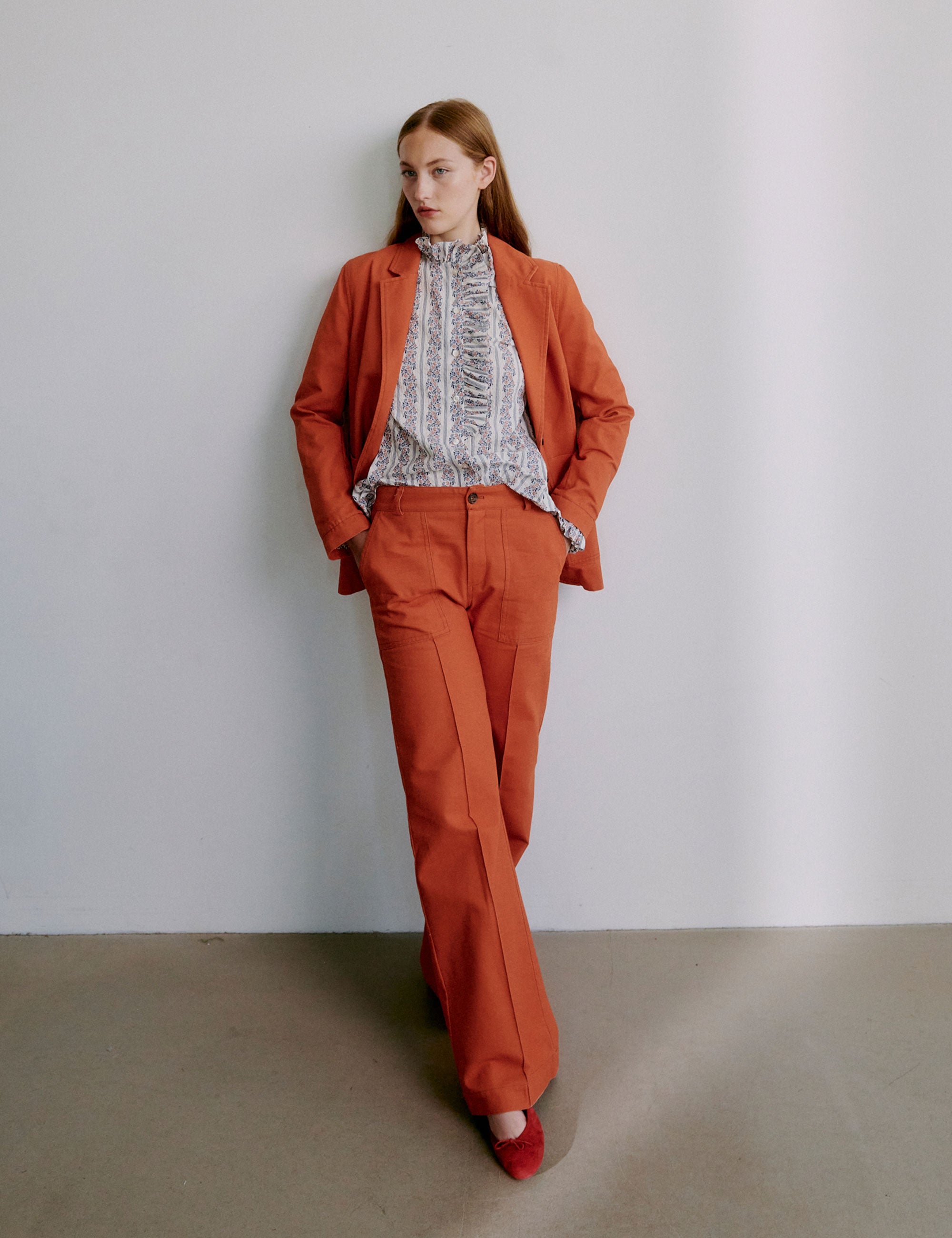 Woman wearing an orange blazer and matching pants with a frilled shirt beneath