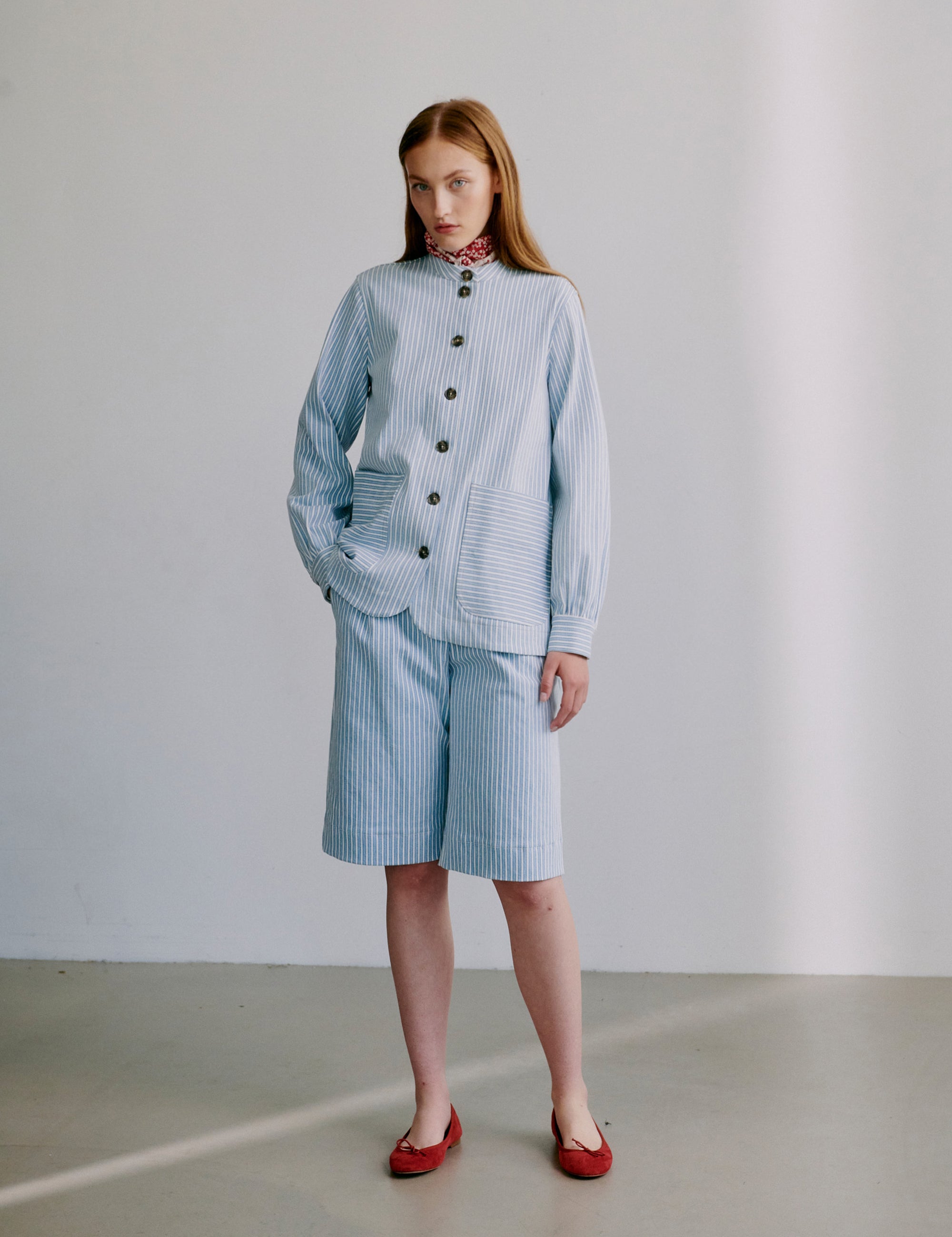 Woman wearing a light blue striped jacket with matching shorts and red shoes on a plain background