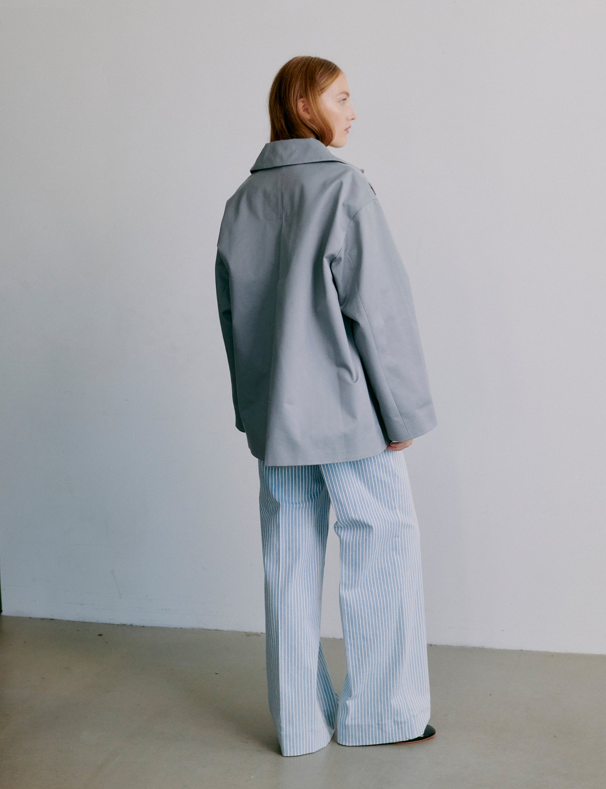 Woman wearing a gray jacket and light blue striped pants against a plain background
