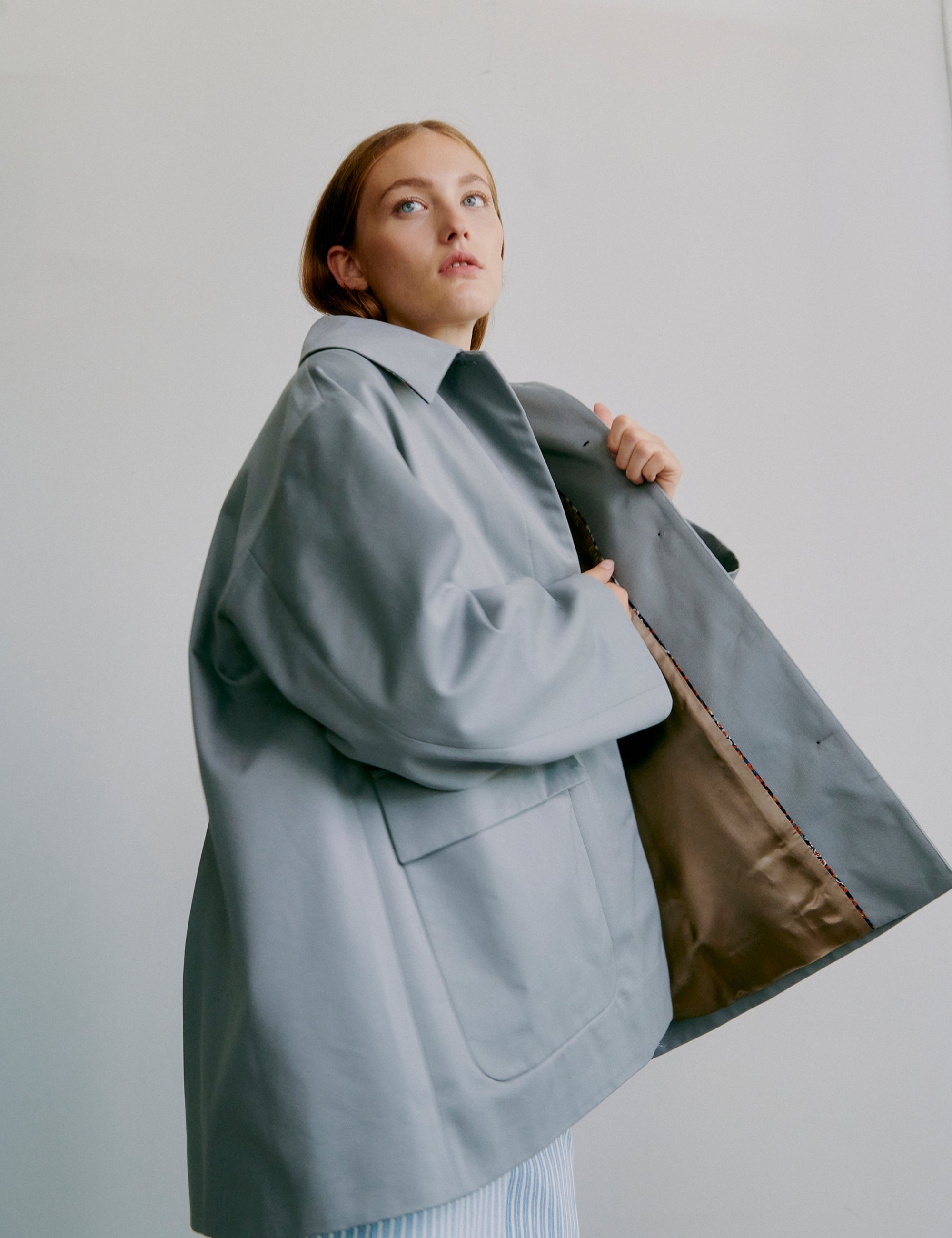 Woman wearing a gray jacket and light blue striped pants against a plain background