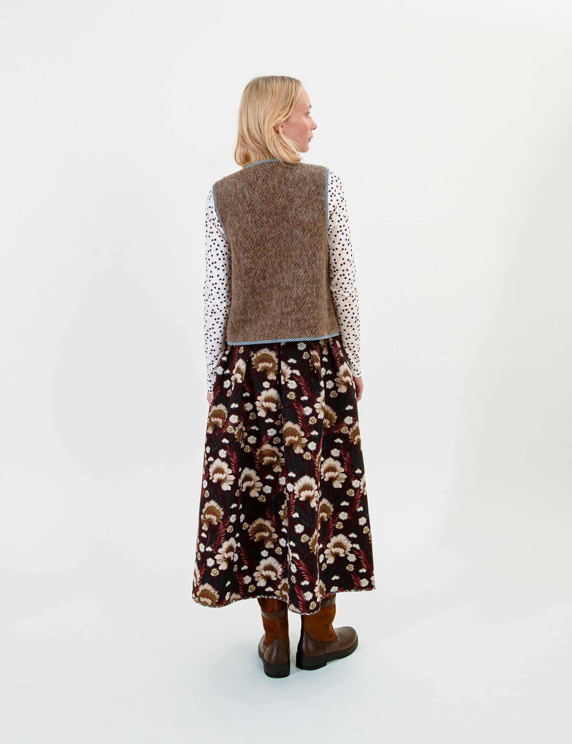 Woman wearing a patterned dress and brown vest on a white background